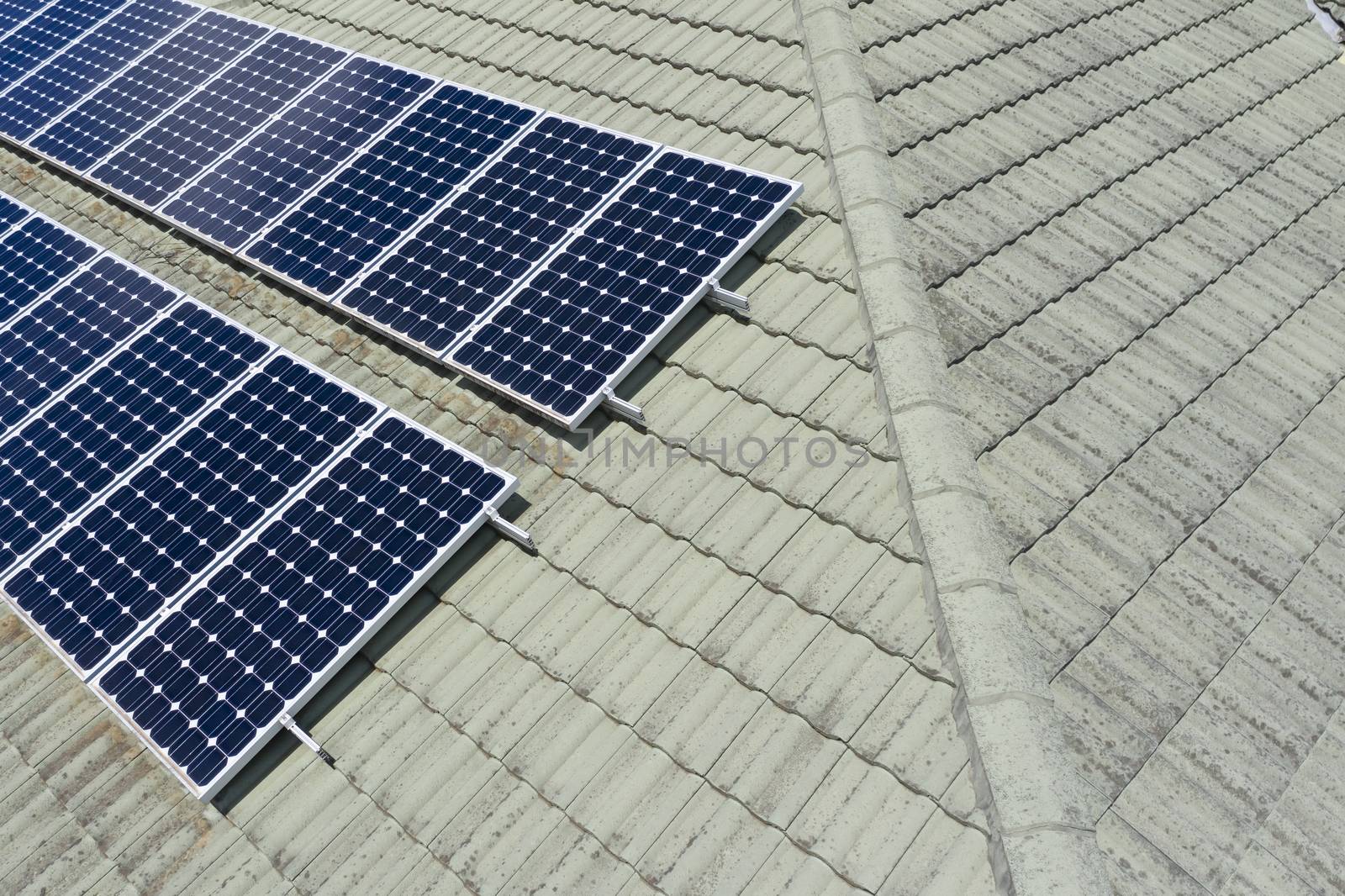 Blue solar panels on a green tiled roof in the bright sunshine.