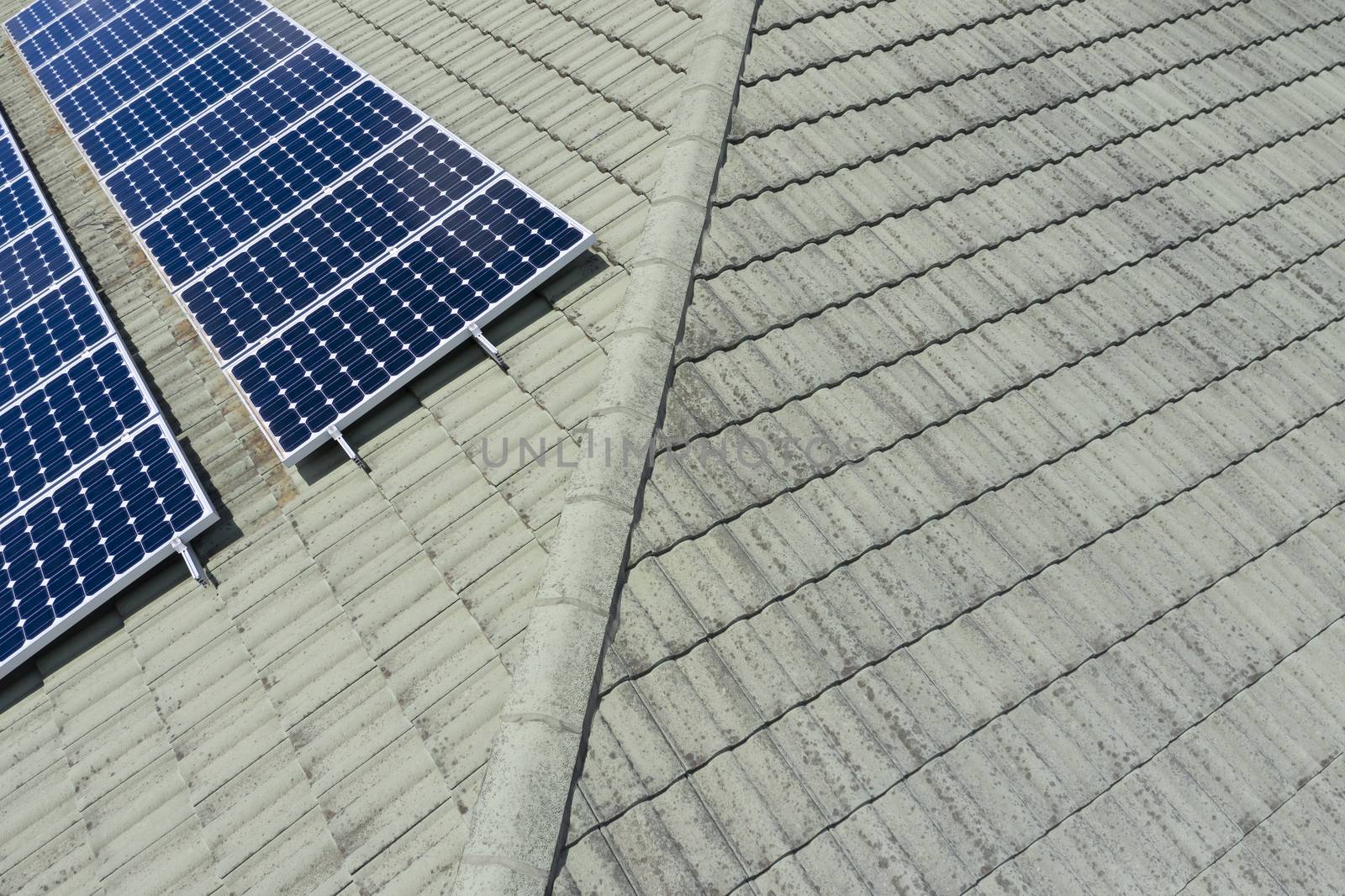 Blue solar panels on a green tiled roof in the bright sunshine.