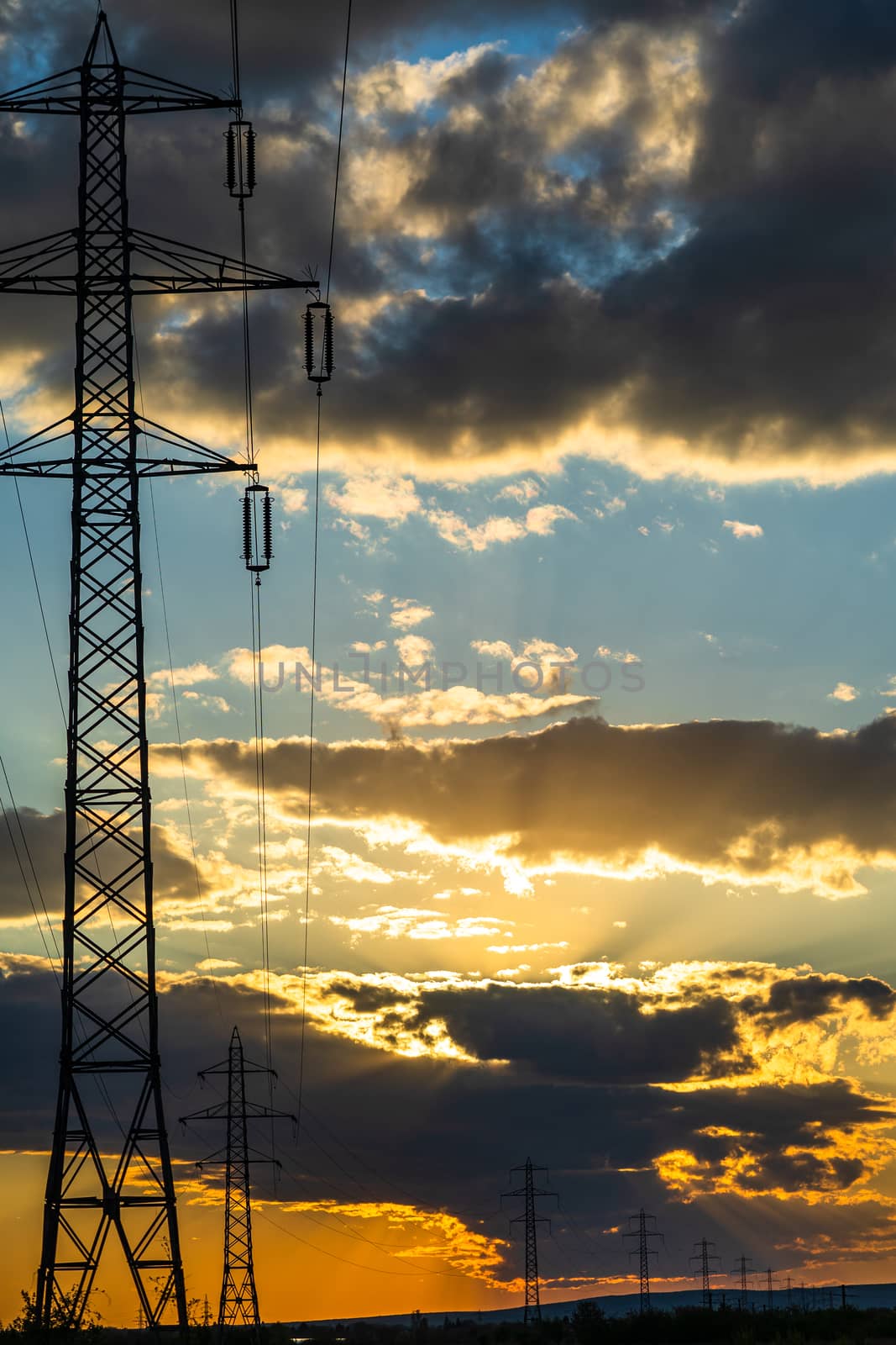 Beautiful dramatic sky and clouds, sunset lights over the transmission tower (electricity pylon) on a field.