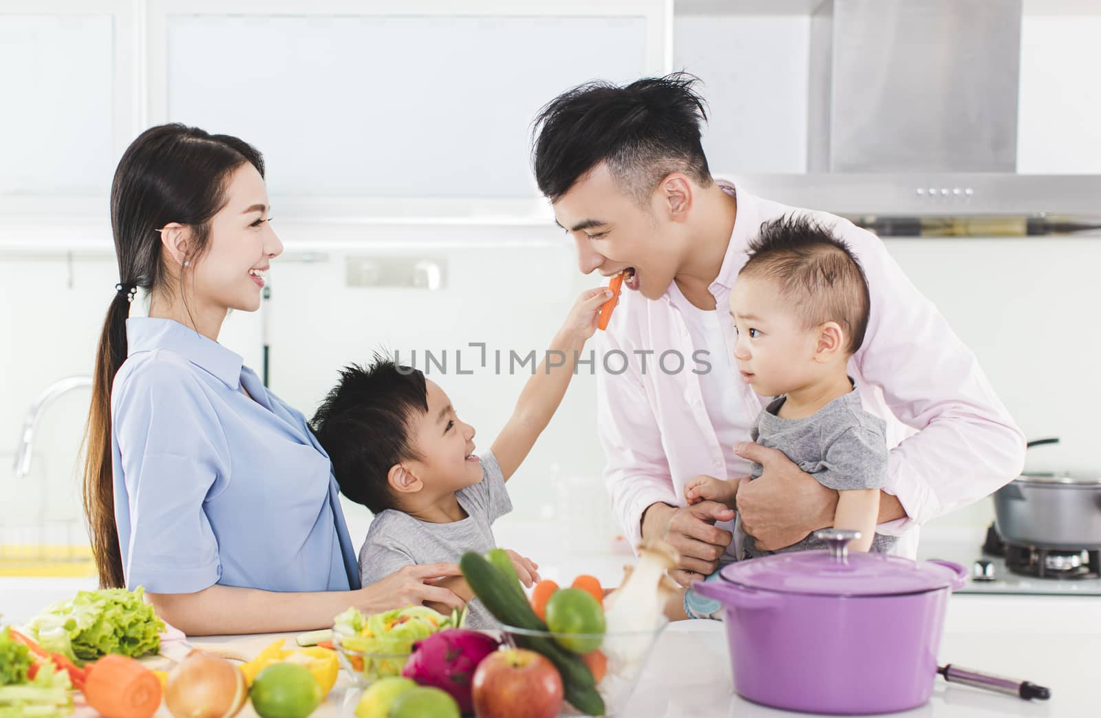 happy little boy feeding father a piece of carrot in kitchen by tomwang