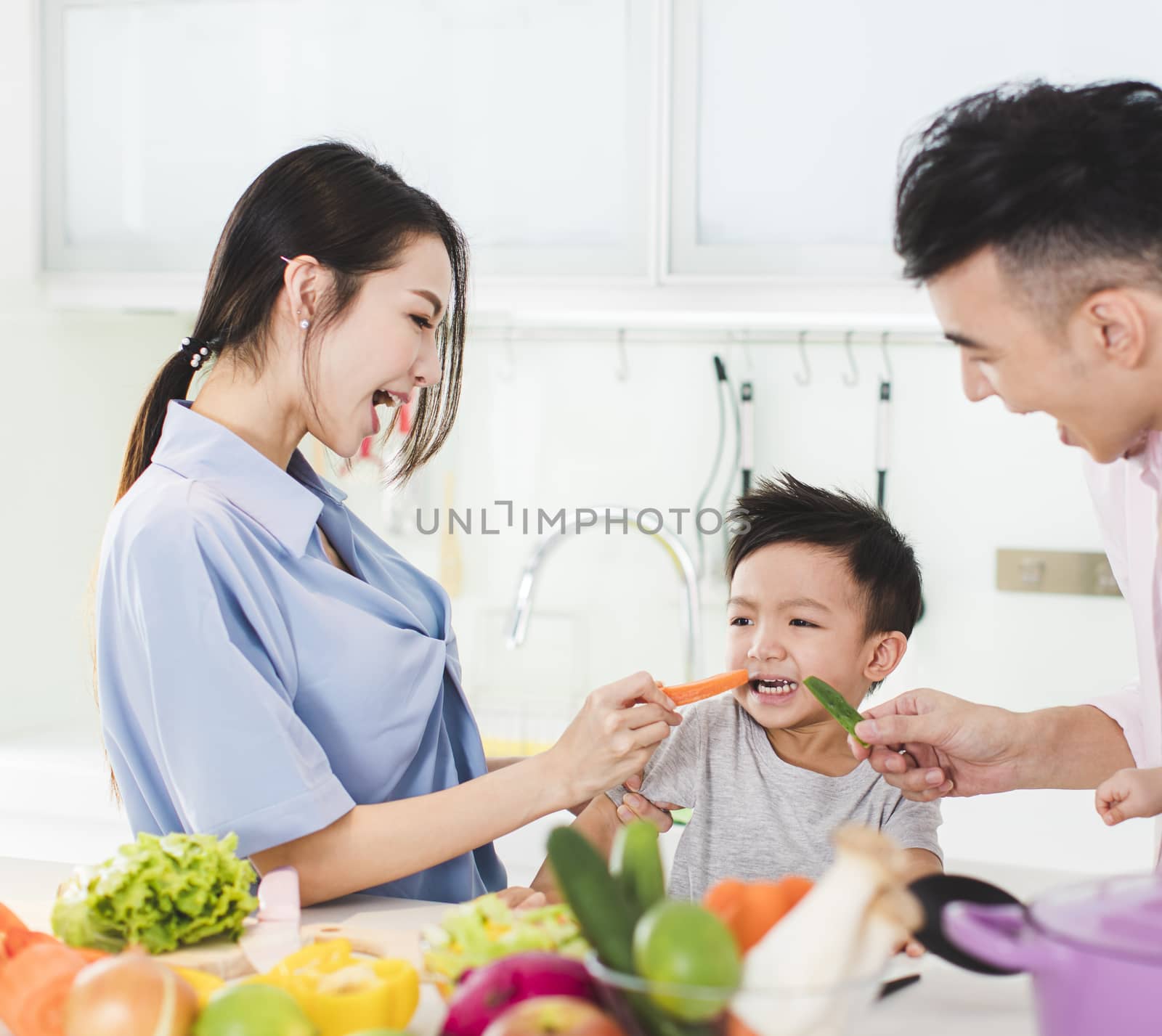 parent feeding boy a piece of carrot in kitchen by tomwang