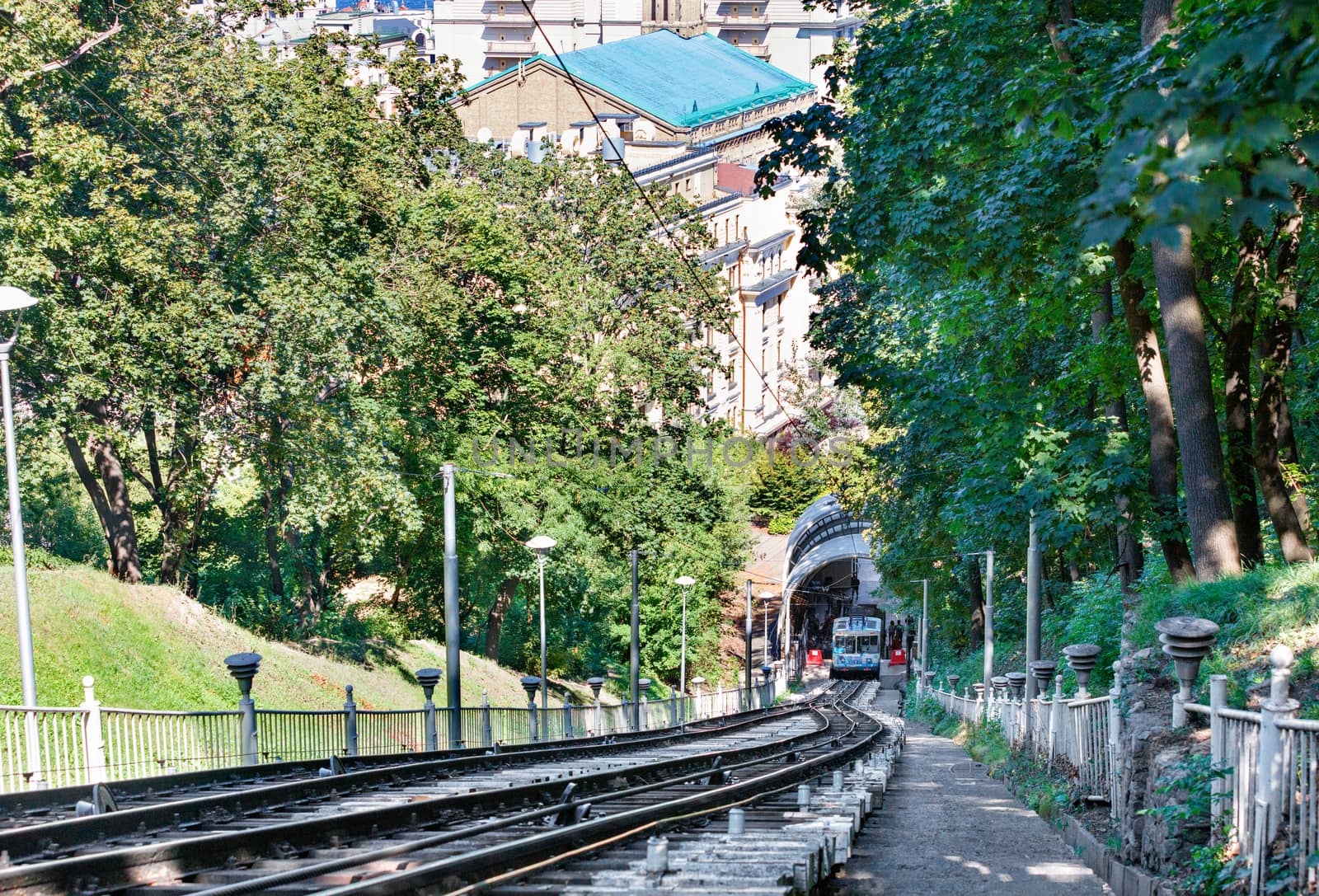 A cable funicular, surrounded by the green foliage of a summer park, picks up passengers at the bottom station to lift them up the mountainside.