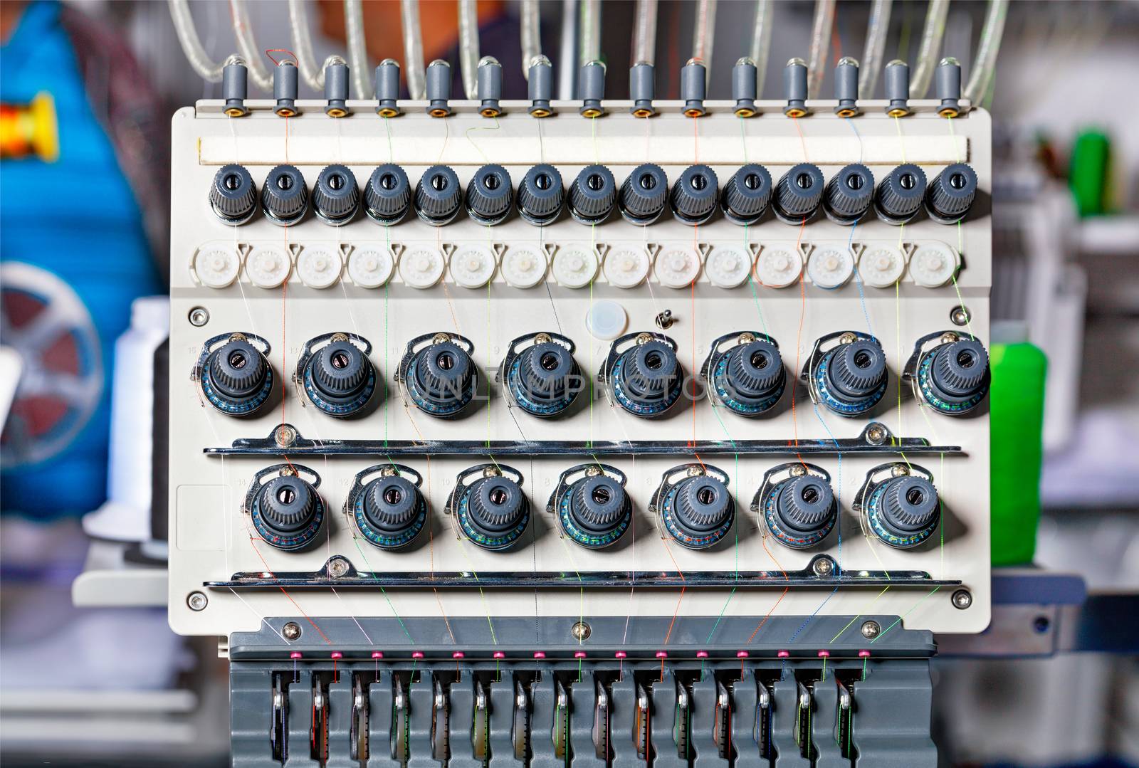 A thread tension control unit at an industrial embroidery machine with multicolored threads, close-up. by Sergii