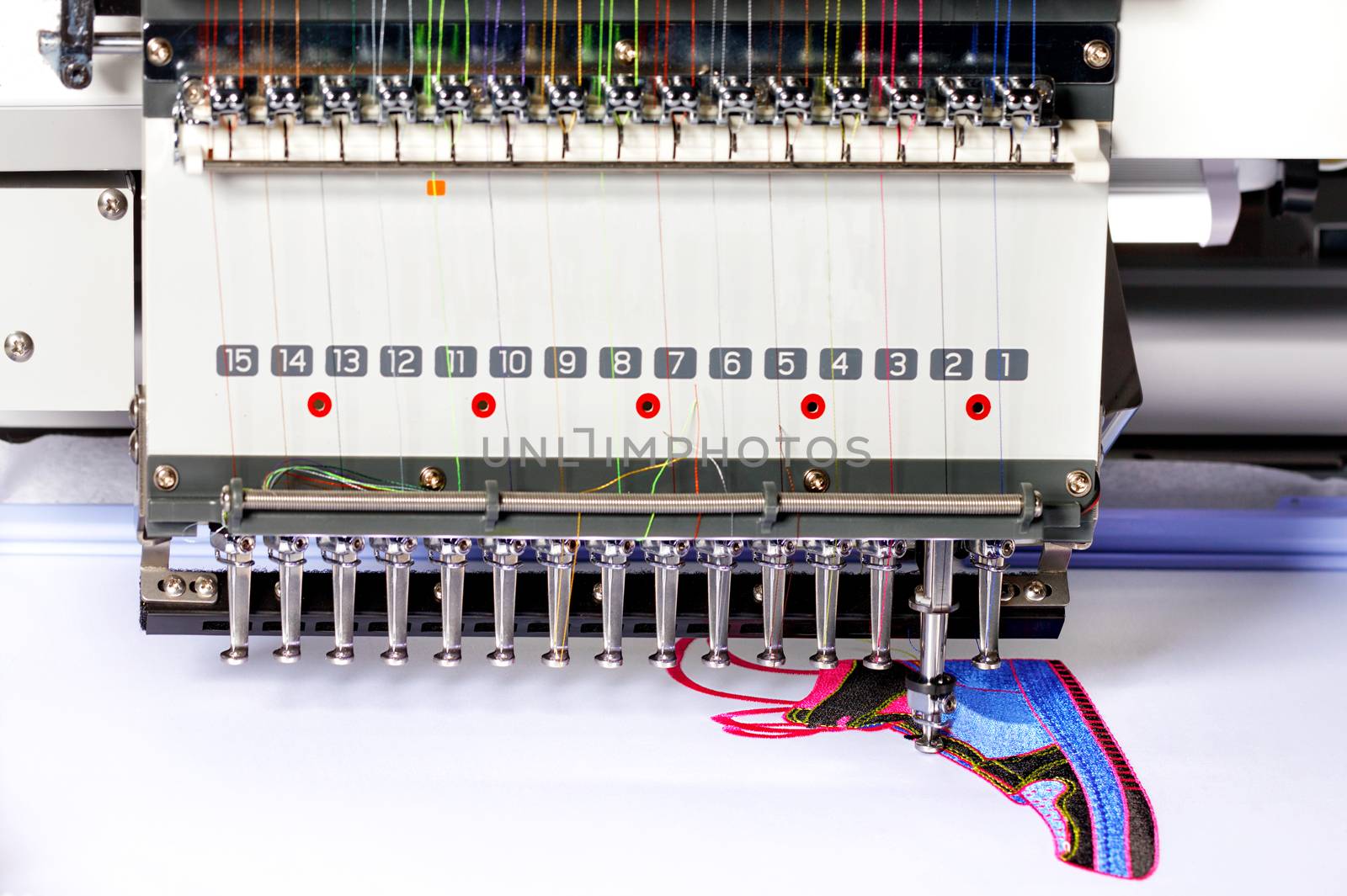 Industrial embroidery machine with multicolored threads, close-up, selective focus. by Sergii