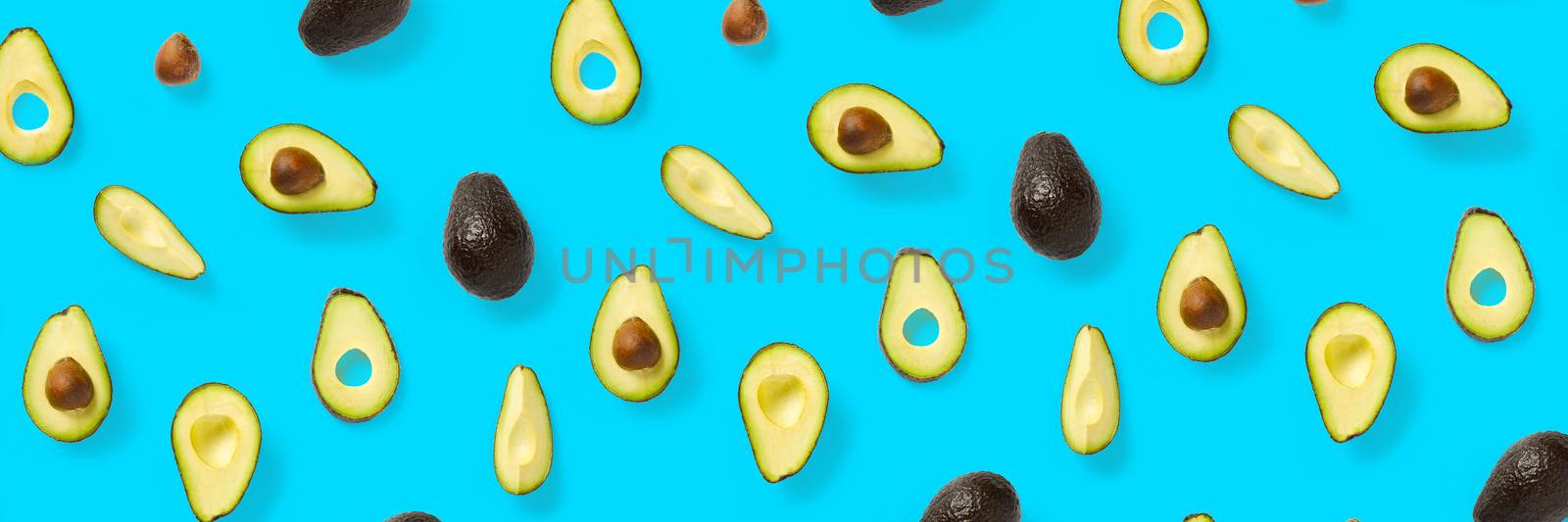 Avocado banner. Background made from isolated Avocado pieces on blue background. Flat lay of fresh ripe avocados and avacado pieces. by PhotoTime