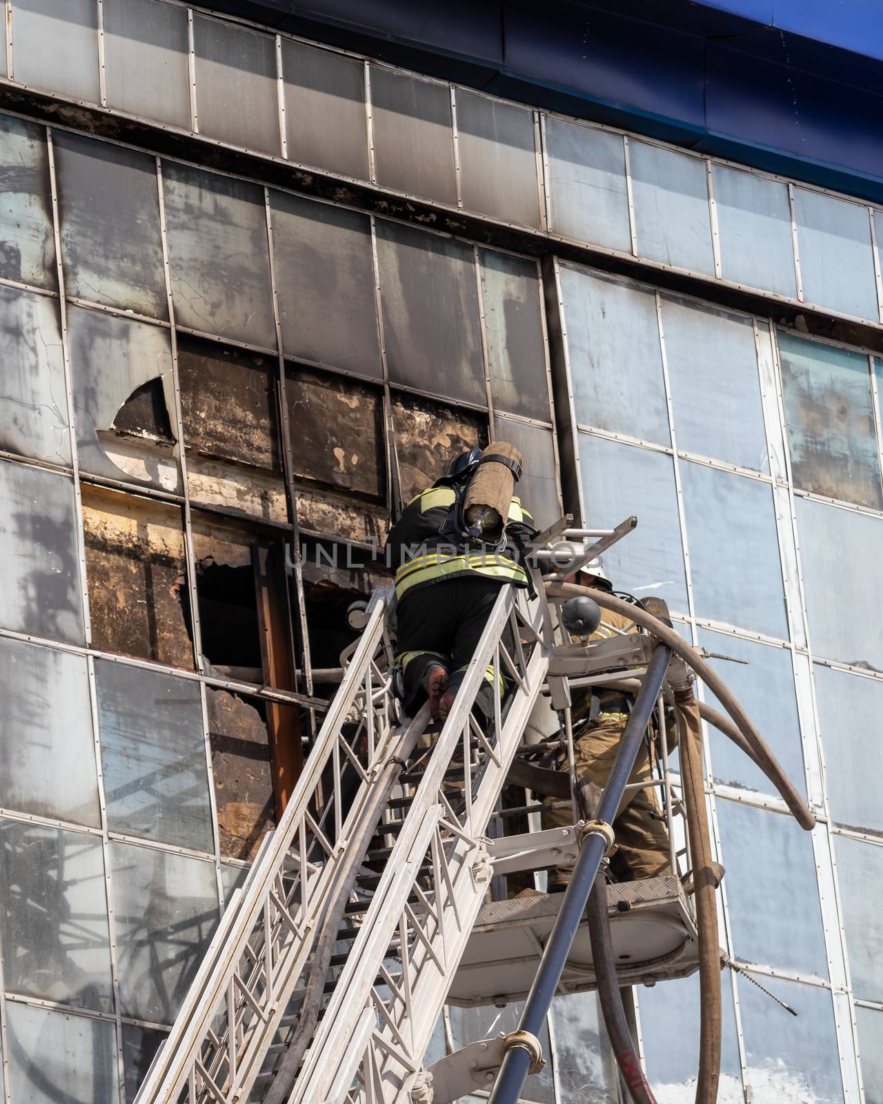 Russia, Kaluga - SEPTEMBER 08, 2020: A team of firefighters in protective suits and helmets on the stairs extinguishing a fire in a building with a broken window and blue roof.