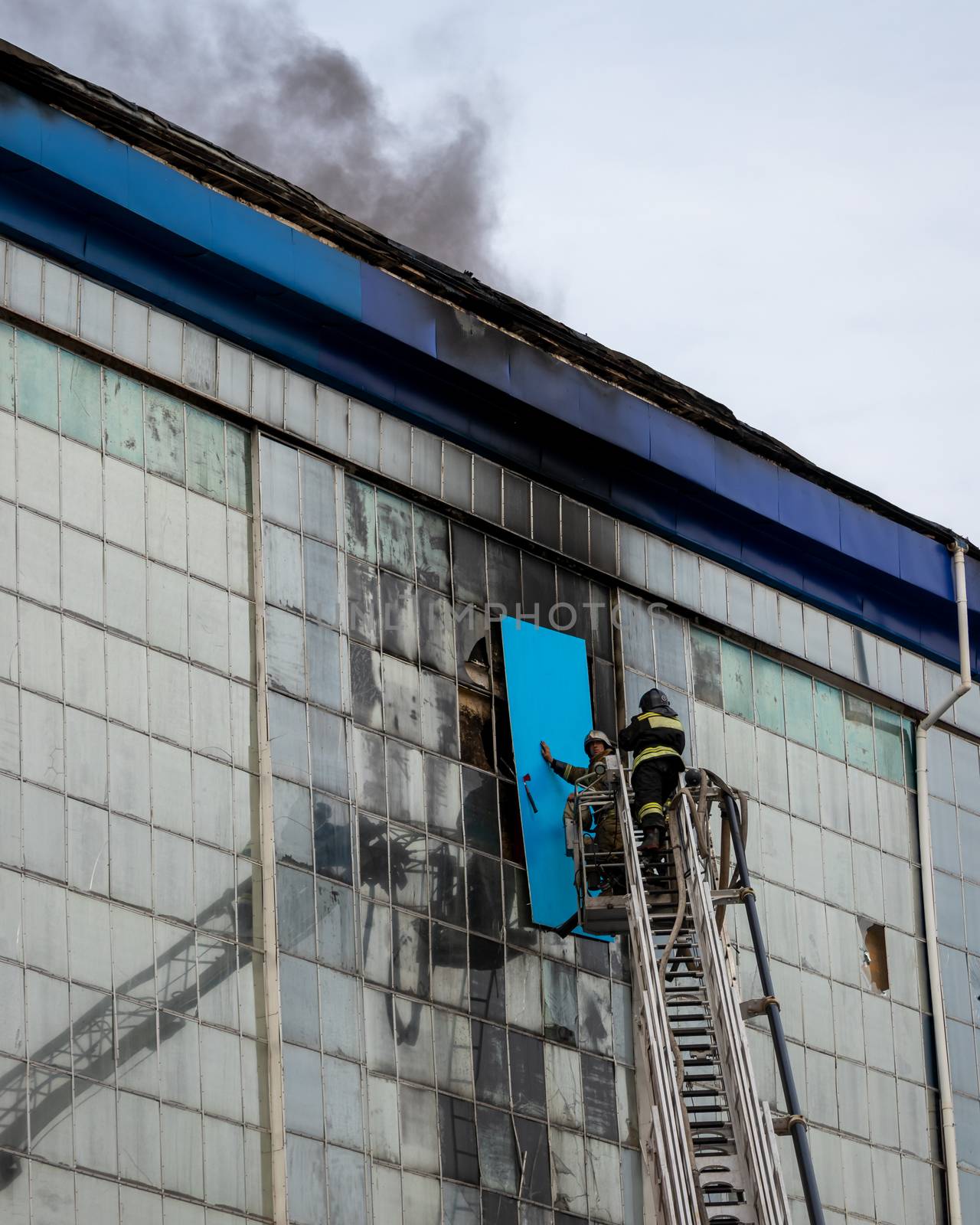 Russia, Kaluga - SEPTEMBER 08, 2020: A team of firefighters in protective suits and helmets on the stairs extinguishing a fire in a building with a broken window and blue roof.