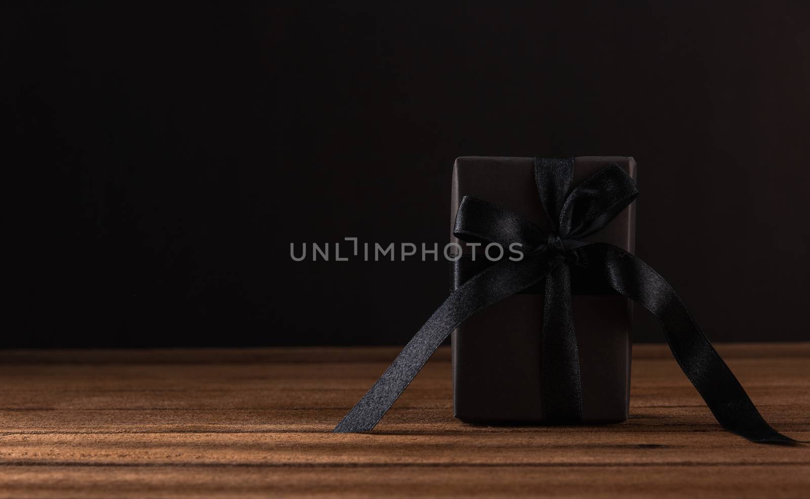 Black Friday sale concept, Gift box wrapped in black paper and black bow ribbon on wooden table studio shot on black background