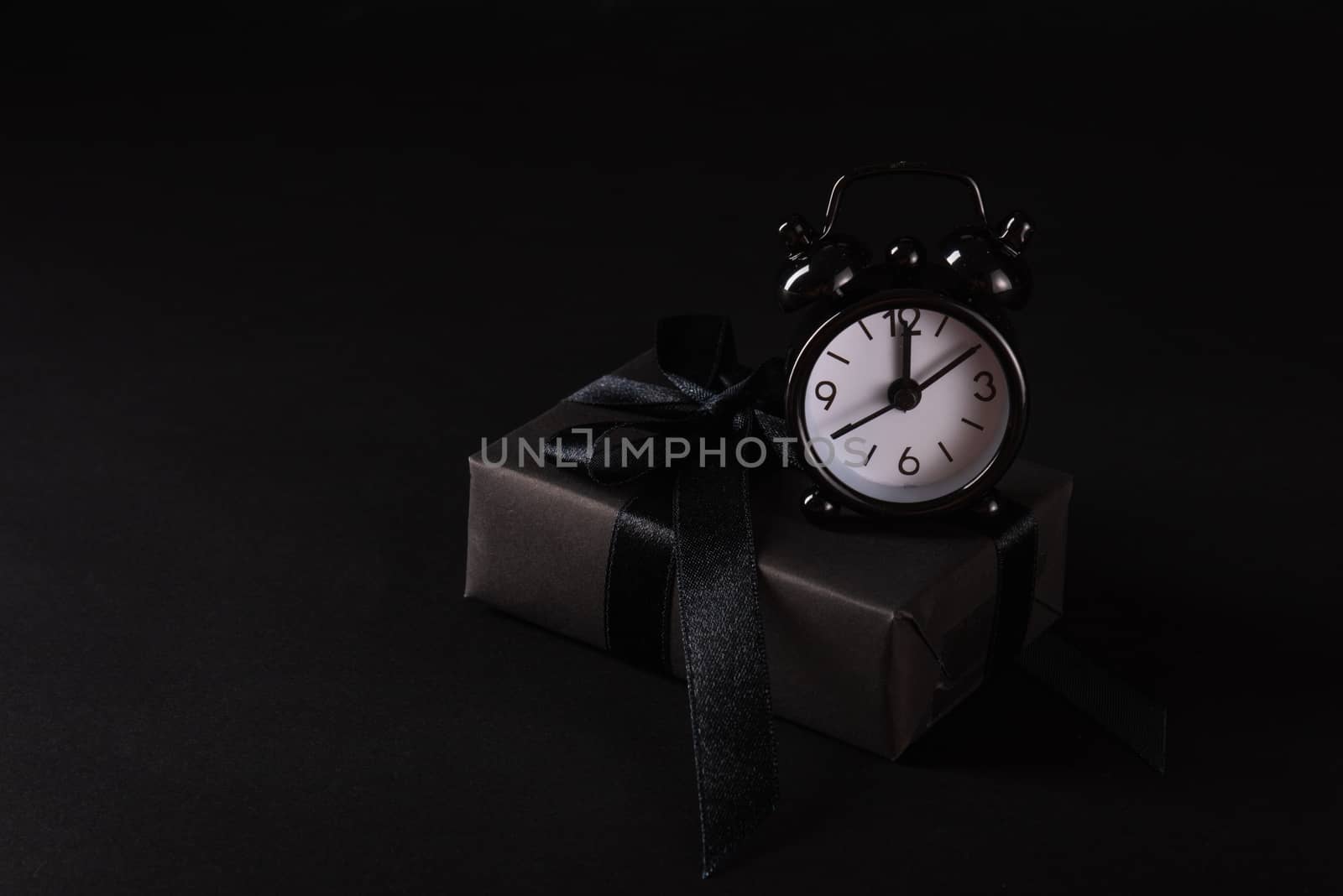 Black Friday sale shopping concept, Top view of gift box wrapped in black paper and black bow ribbon and black alarm clock, studio shot on black background