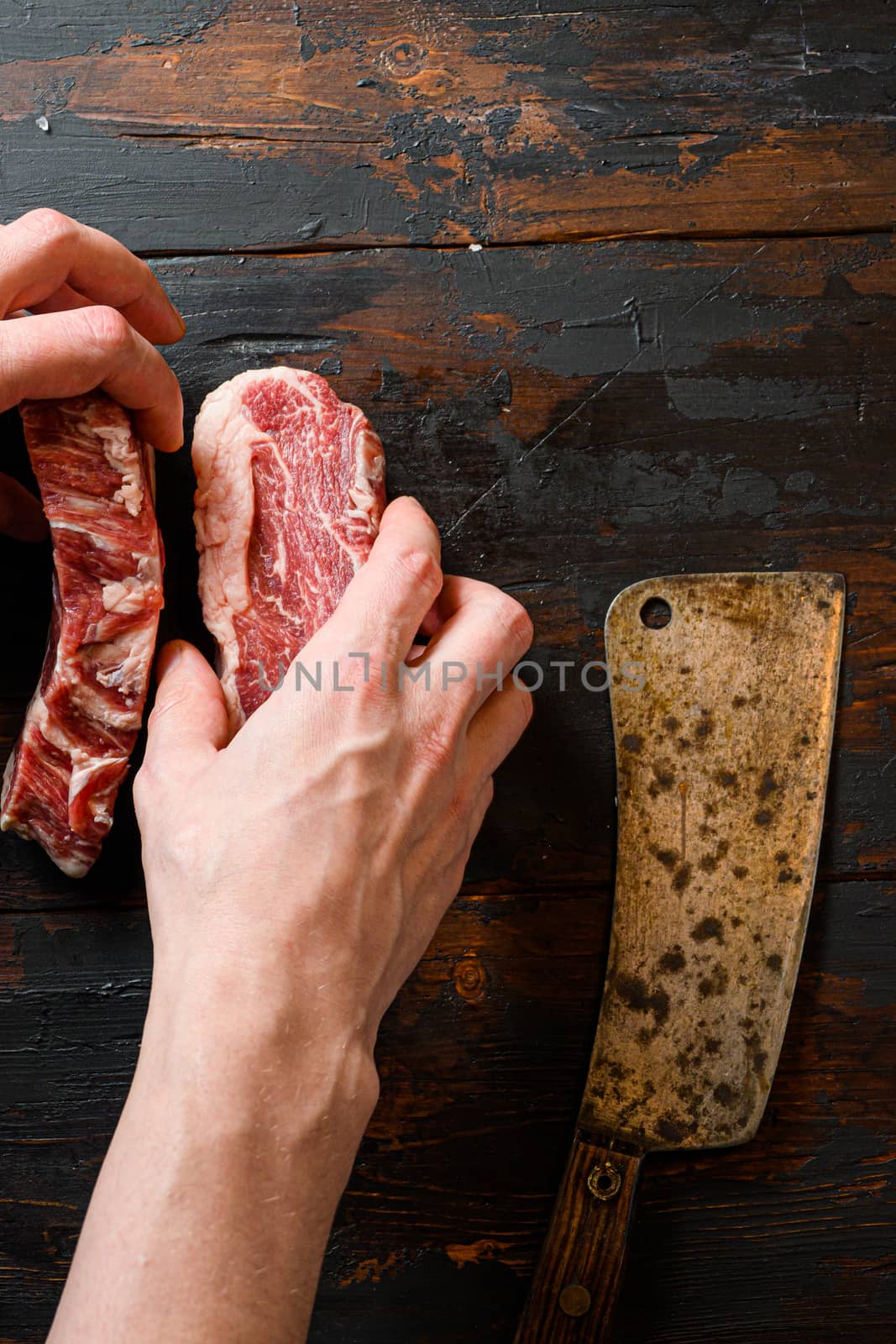 Fresh Chuck eye roll black angus marbled beef steak on vintage dark wood table Organic beef. with butcher hands and meat cleaver at work by Ilianesolenyi