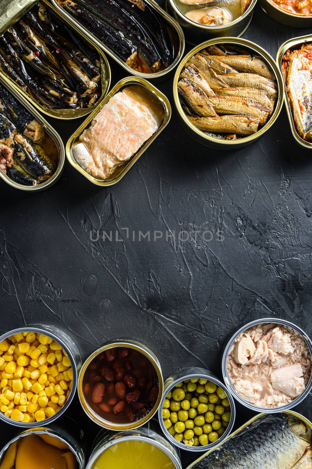 Canned conserve products in tin cans. with fresh organic ingridients Saury, mackerel, sprats, sardines, pilchard, squid, tuna pinapple, corn, peas, mango , beans, over black stone textured background top view copyspace side by side vertical center text concept by Ilianesolenyi