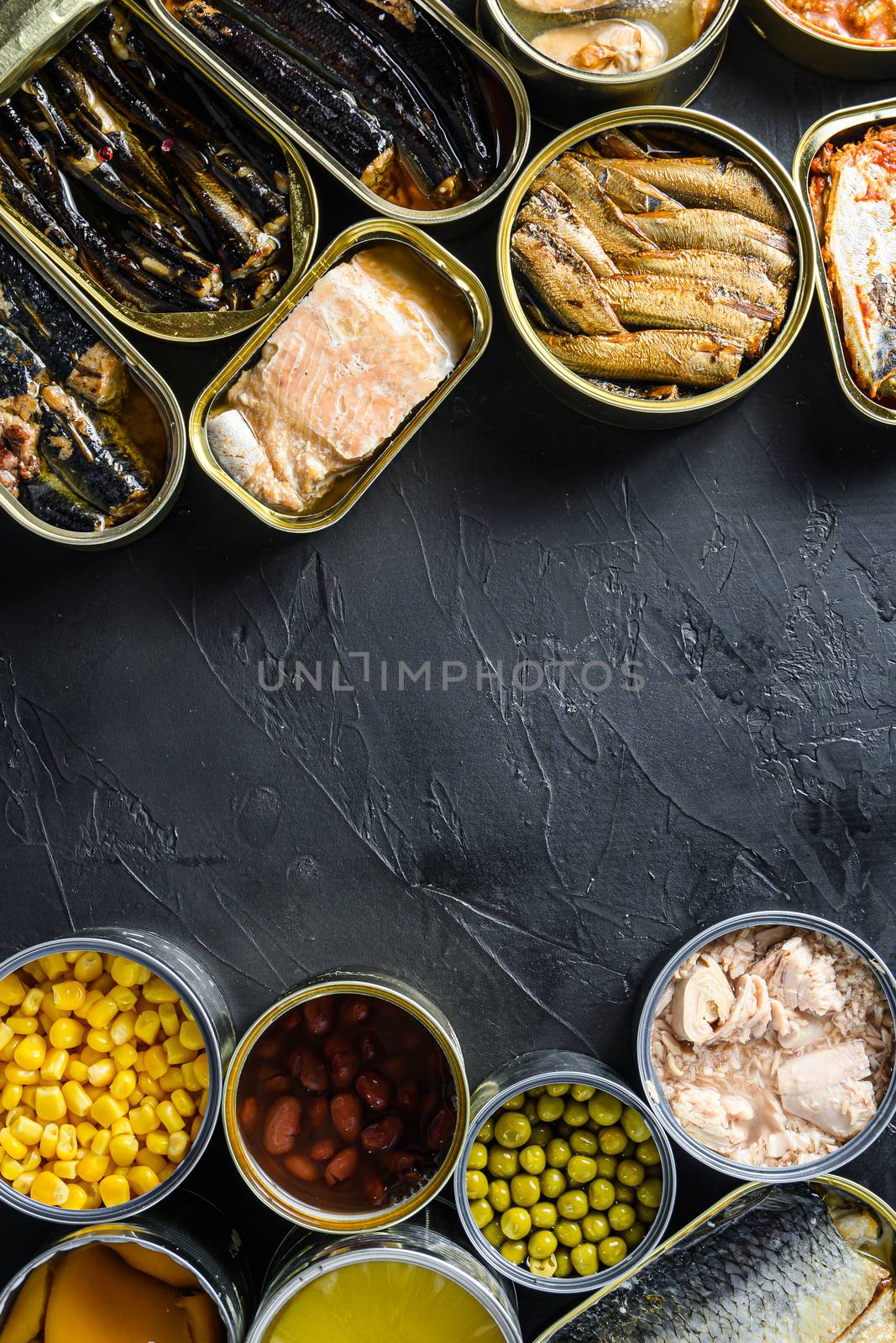 Canned conserve products in tin cans. with fresh organic ingridients Saury, mackerel, sprats, sardines, pilchard, squid, tuna pinapple, corn, peas, mango , beans, over black stone textured background top view copyspace side by side vertical center text concept.