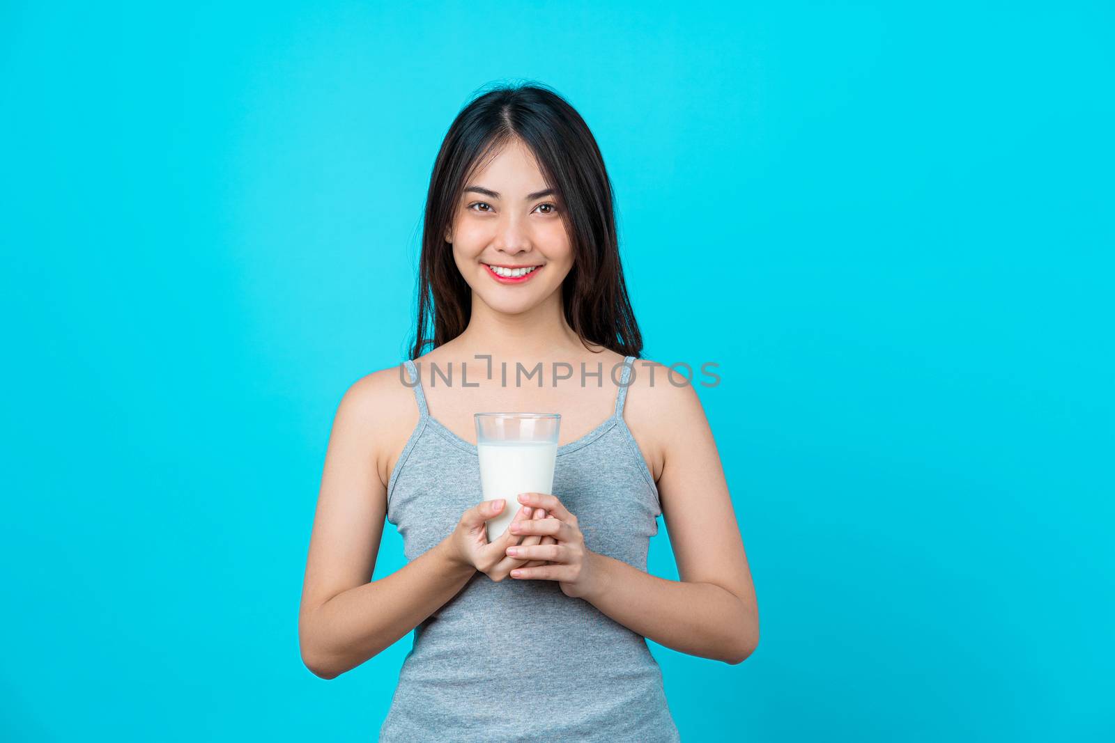 Attractive Asian young woman holding milk on isolated blue color background, weight loss and avoid junk food for dieting and Healthy