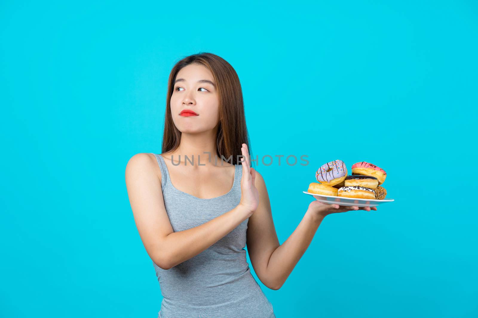 Attractive Asian young woman doing no action with donuts on isolated blue color background, weight loss and avoid junk food for dieting and Healthy concept, copy space and studio