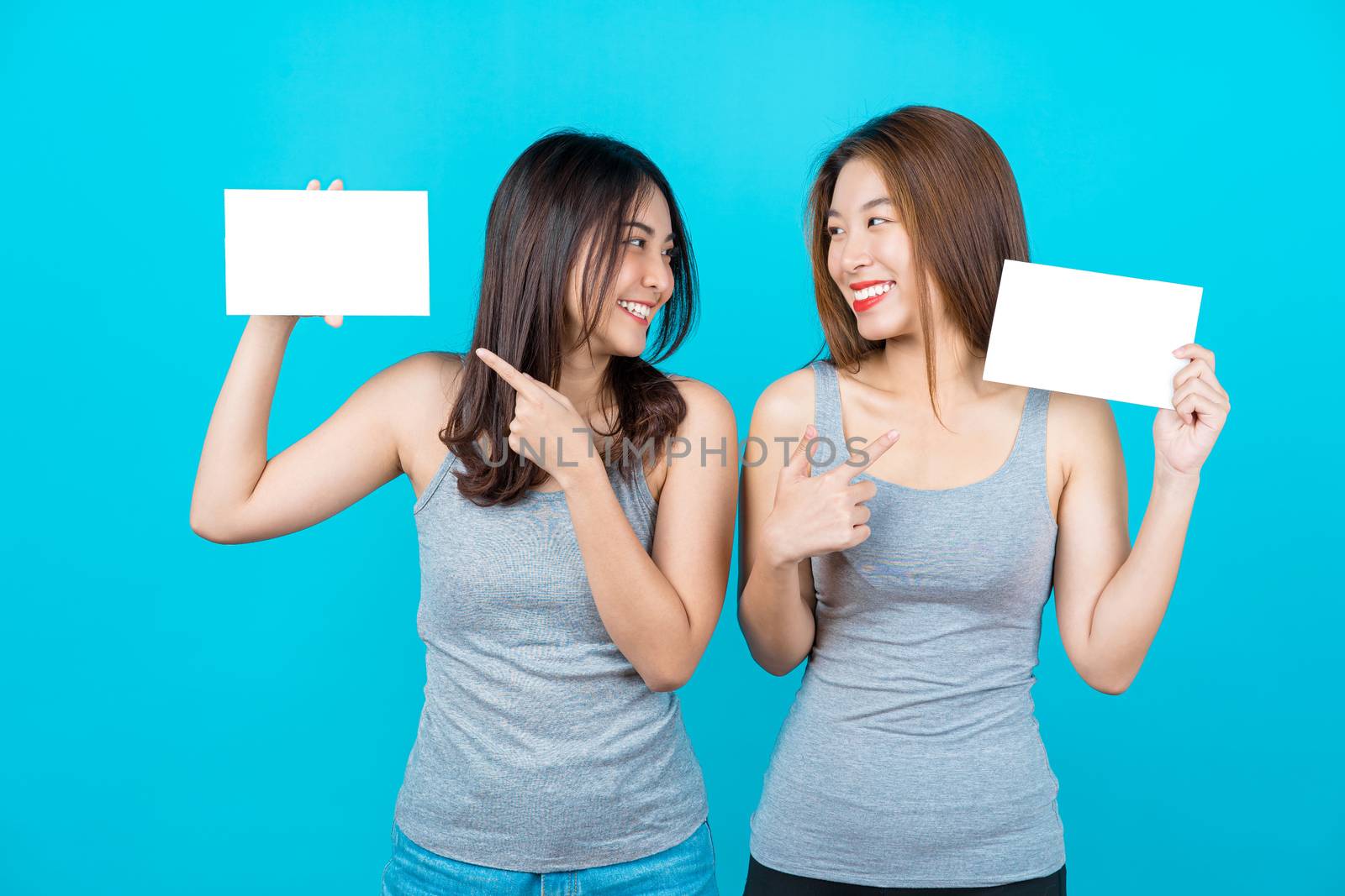 Two Asian smiling young women showing and presenting with poster by Tzido