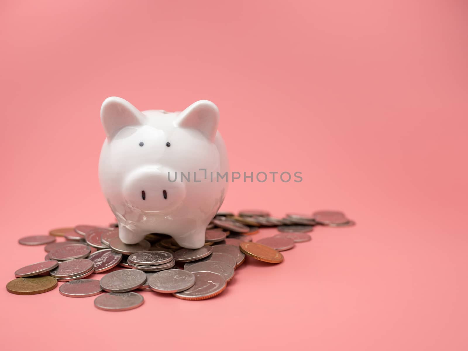 White piggy bank Placed on top of a pile of coins On a pink background. saving money concept.