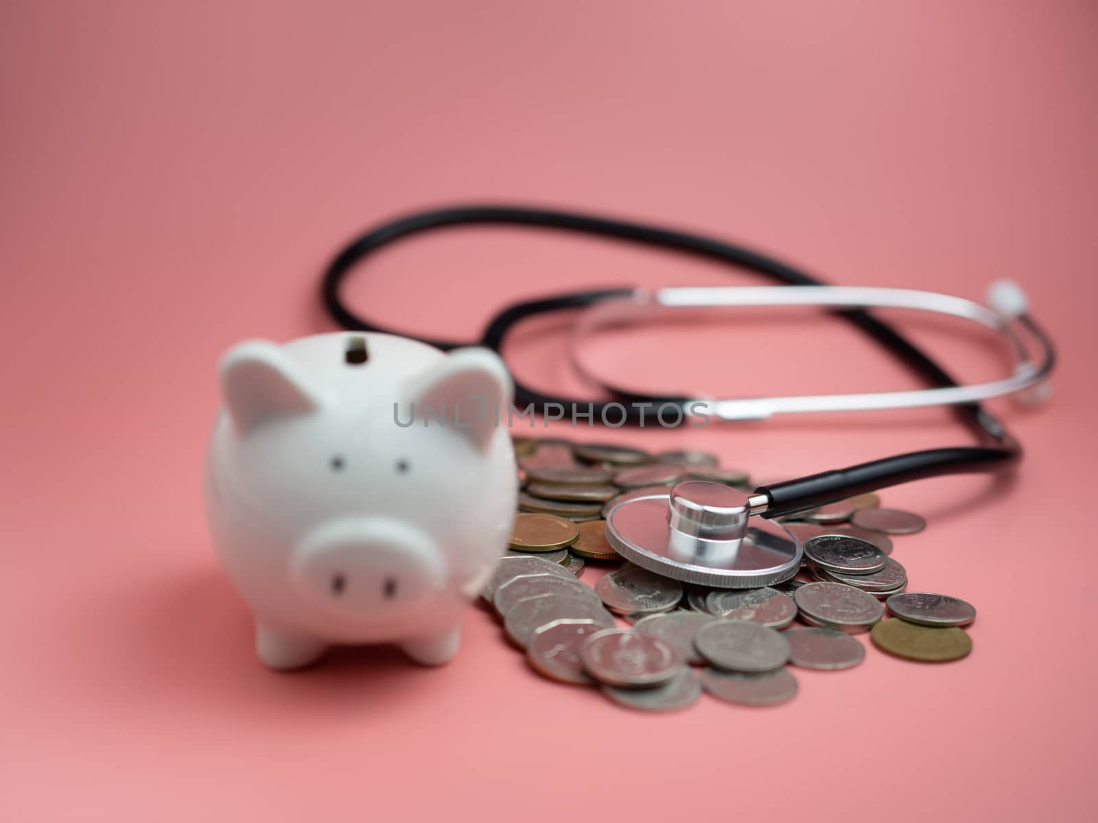 Stethoscope on the pile of money and piggy bank on pink backgrou by Unimages2527