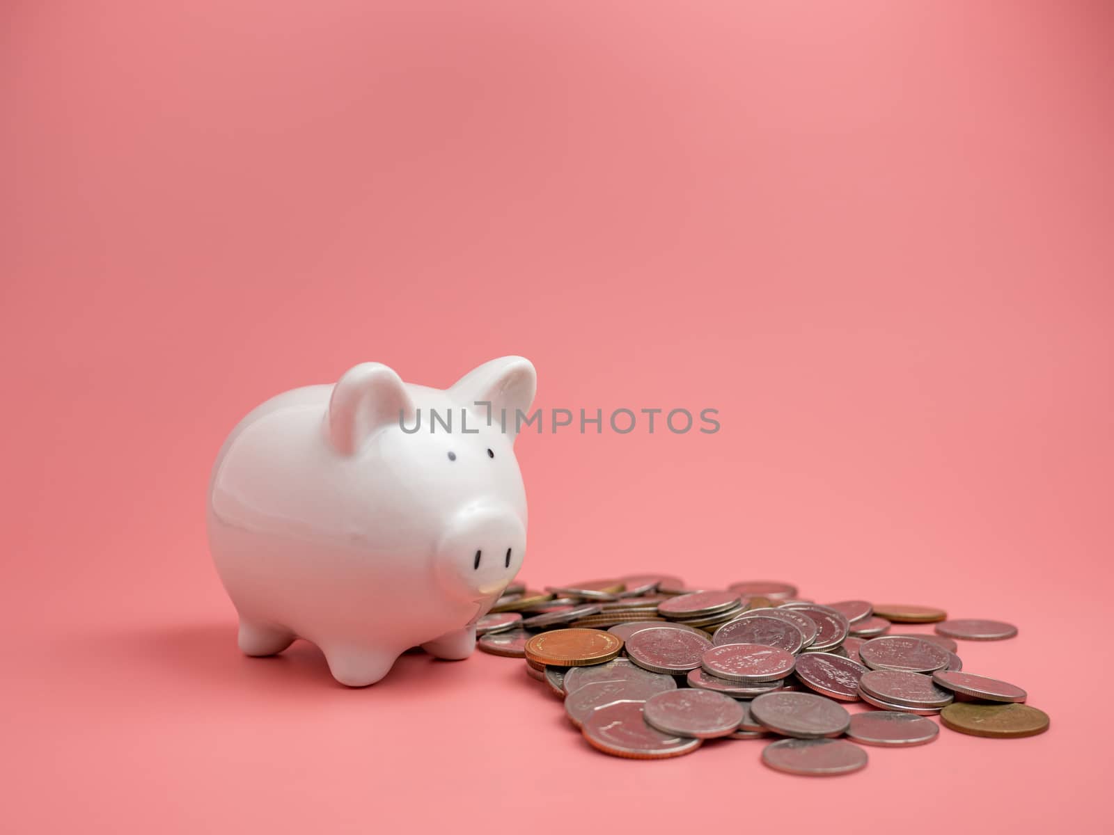 White piggy bank With a pile of coins On a pink background. saving money concept.