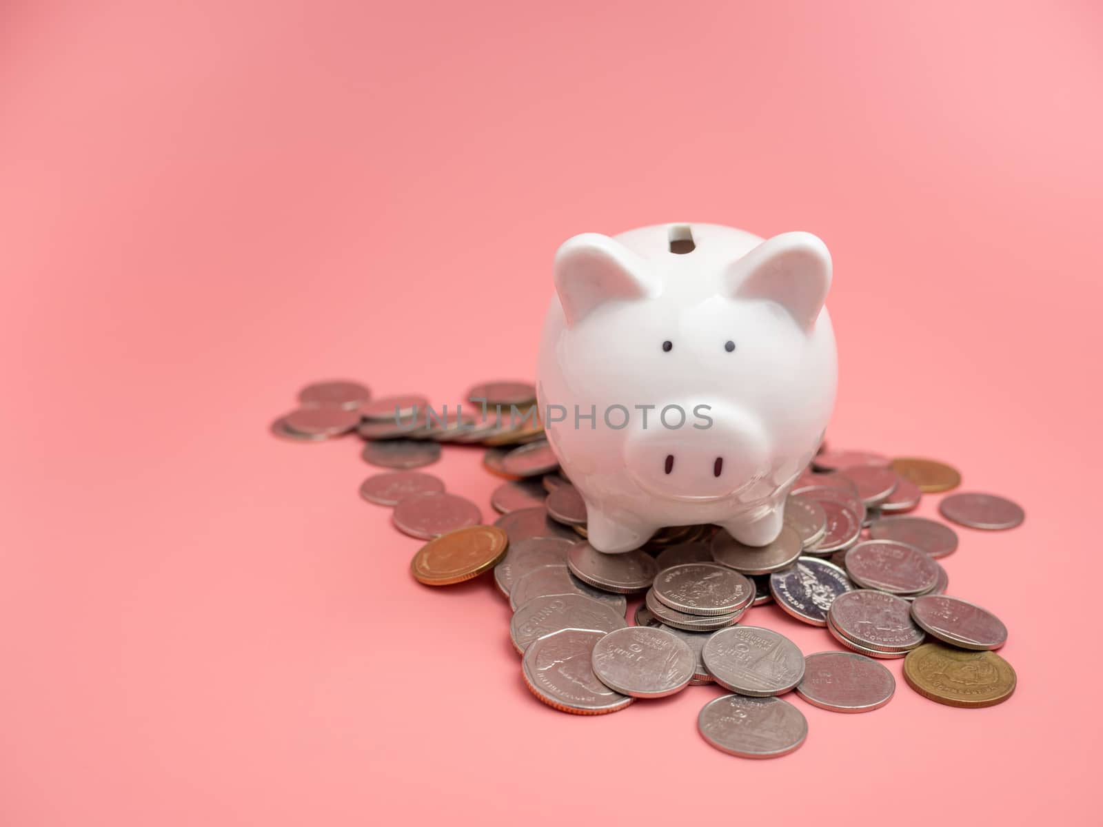 White piggy bank Placed on top of a pile of coins On a pink background. saving money concept.