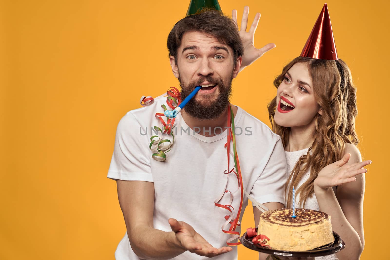 Man and woman birthday festive cake yellow background and caps on the headv by SHOTPRIME