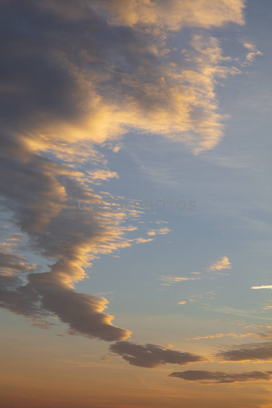 Beautiful dramatic cloudscape with orange and yellow fluffy sunset clouds over blue sky, low angle view