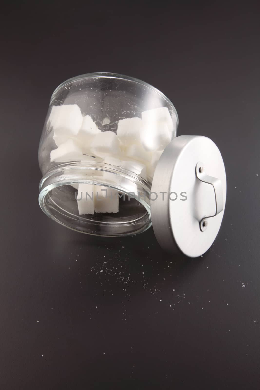 White lump sugar in a glass jar on a gray background, sweet sugar in ware with a glass opened, nobody.