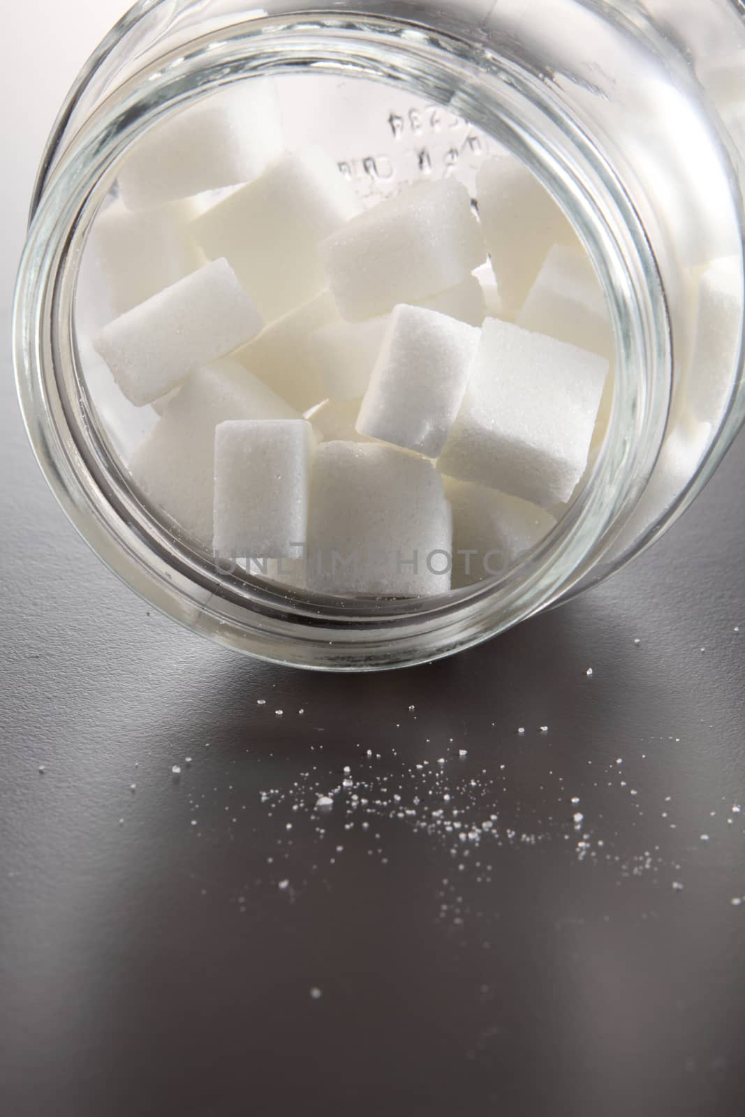 White lump sugar in a glass jar on a gray background, sweet sugar in ware with a glass opened, nobody.