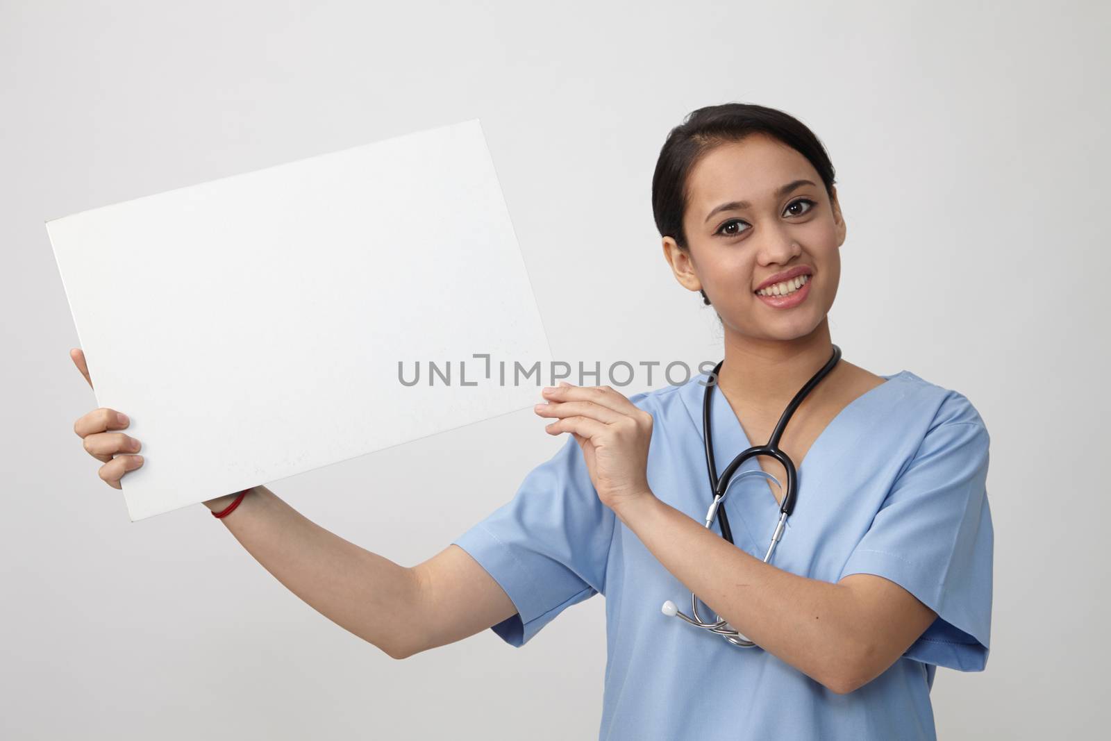 Nurse showing medical sign billboard standing, Young smiling woman nurse or doctor in scrubs showing empty blank sign board with copy space. Indian model isolated on white background