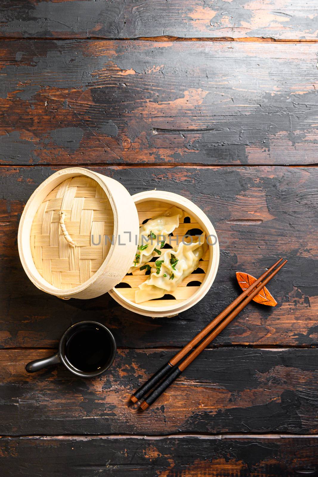 Boiled and hot chinese dumplings in wooden steamer with soy sauce fresh herbs and chopsticks on old wood table top view by Ilianesolenyi