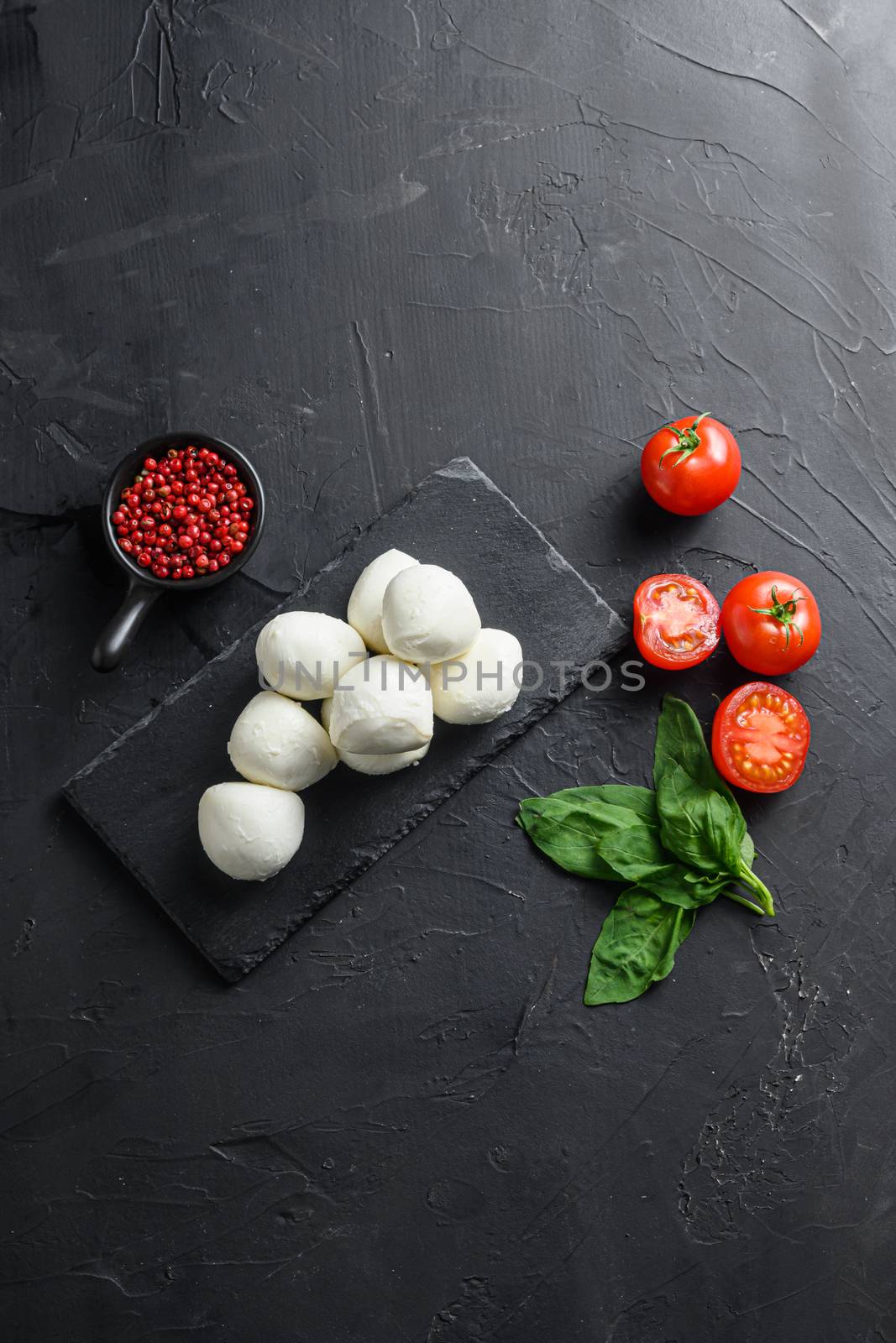 Mozzarella cheese, basil tomato cherry over old black backgroundon black stone slate space for text vertical. by Ilianesolenyi