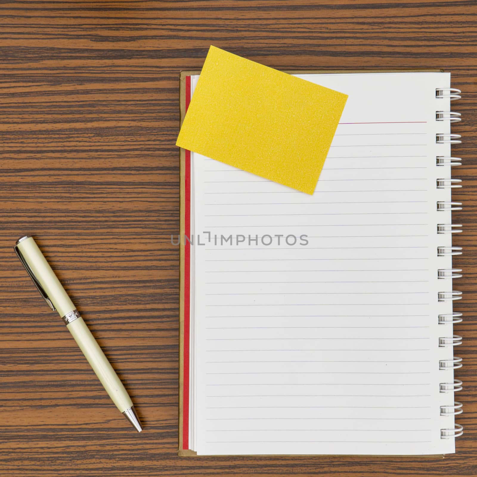 Personal notepad, yellow paper note and a pen on a zebra wood brown striped table. by sonandonures