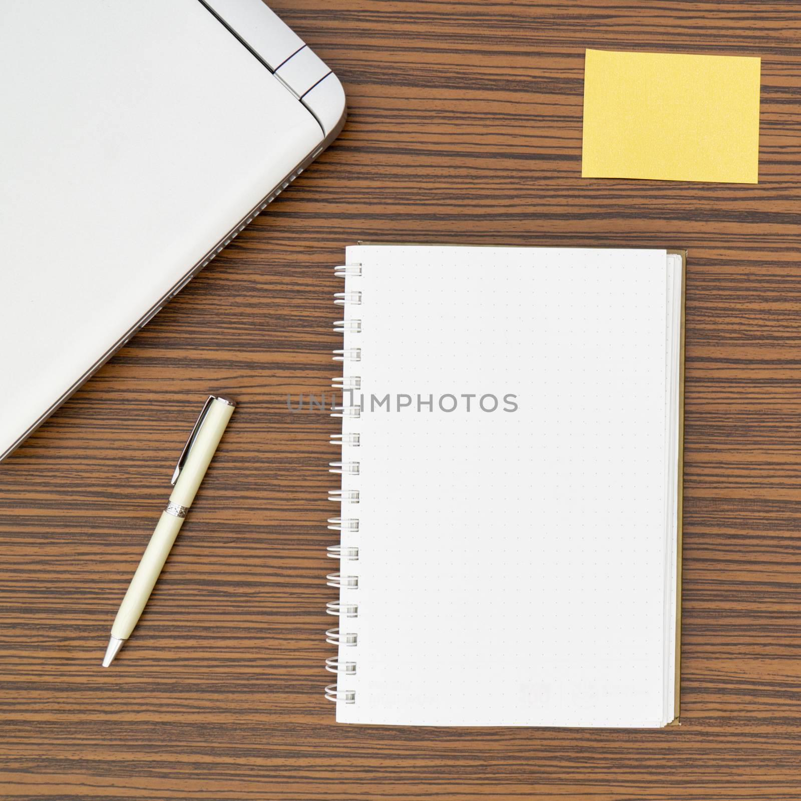 An office table working enviroment. Notepad, sticky note, pen plant, calculator and a lap top on a brown striped zebrawood design table top. Must have objects while working from home during Covid-19 by sonandonures