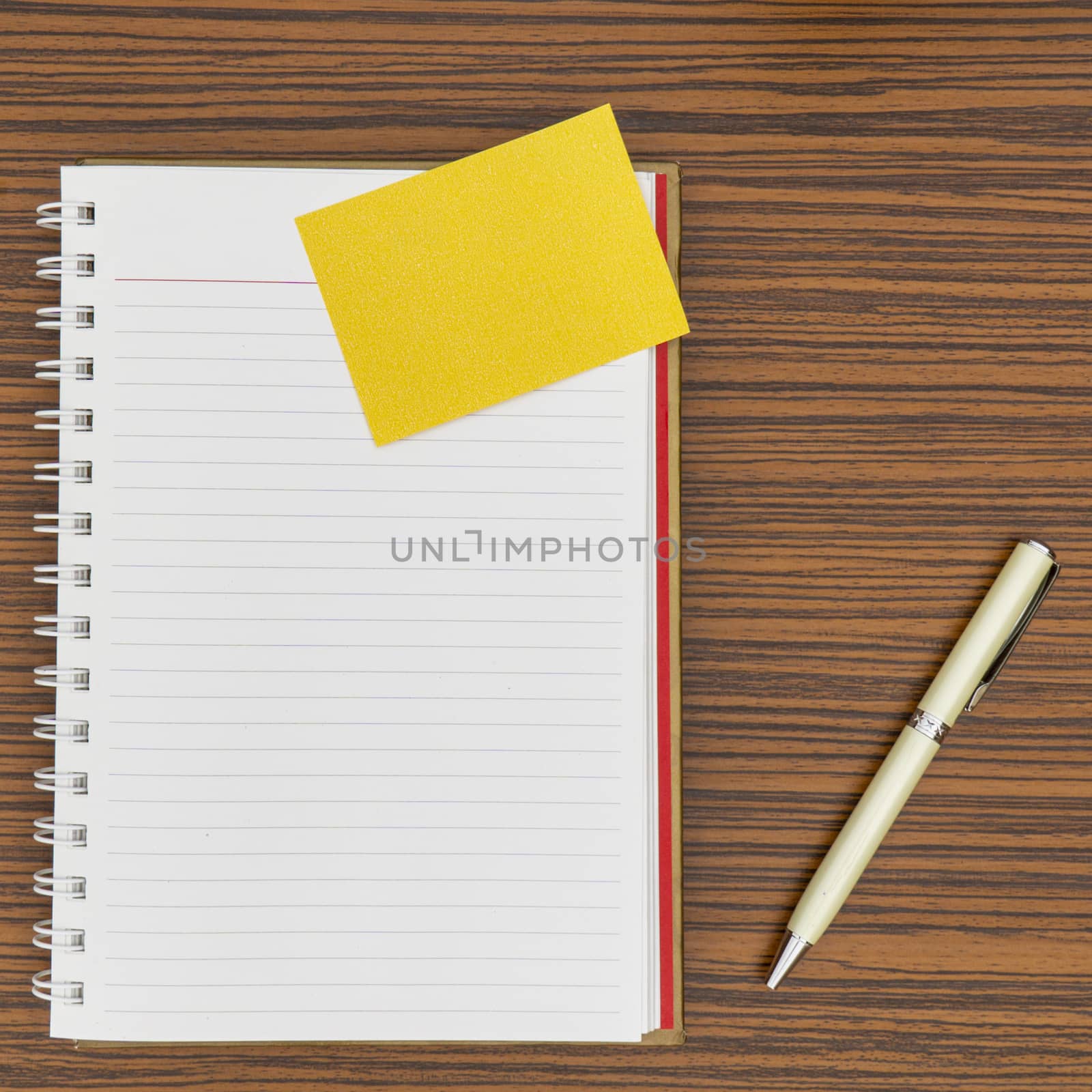 Personal notepad, yellow paper note and a pen on a zebra wood brown striped table.