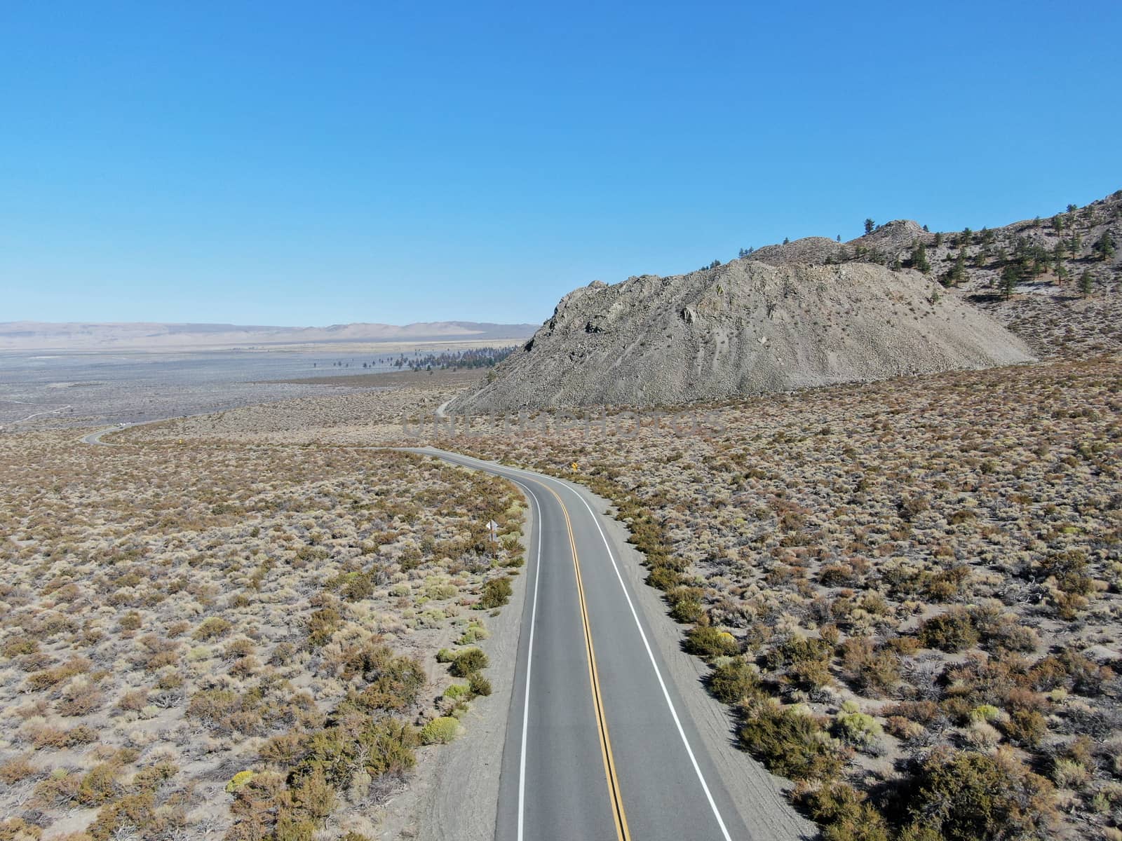 Aerial view of asphalt road in the middle of dusty dry desert land in Lee Vining, Mono County, California, USA