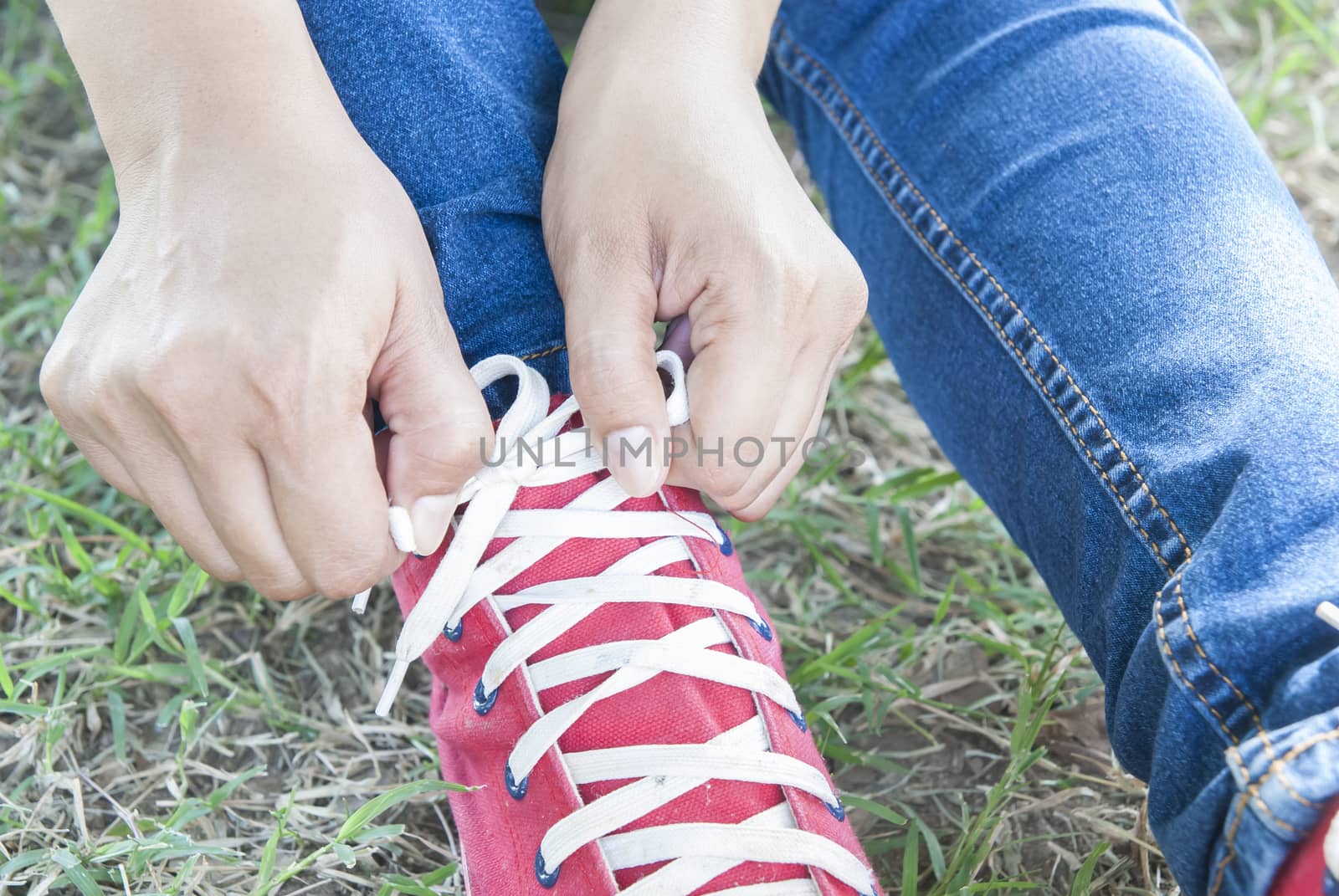 close up of woman tying shoe laces on green glass 