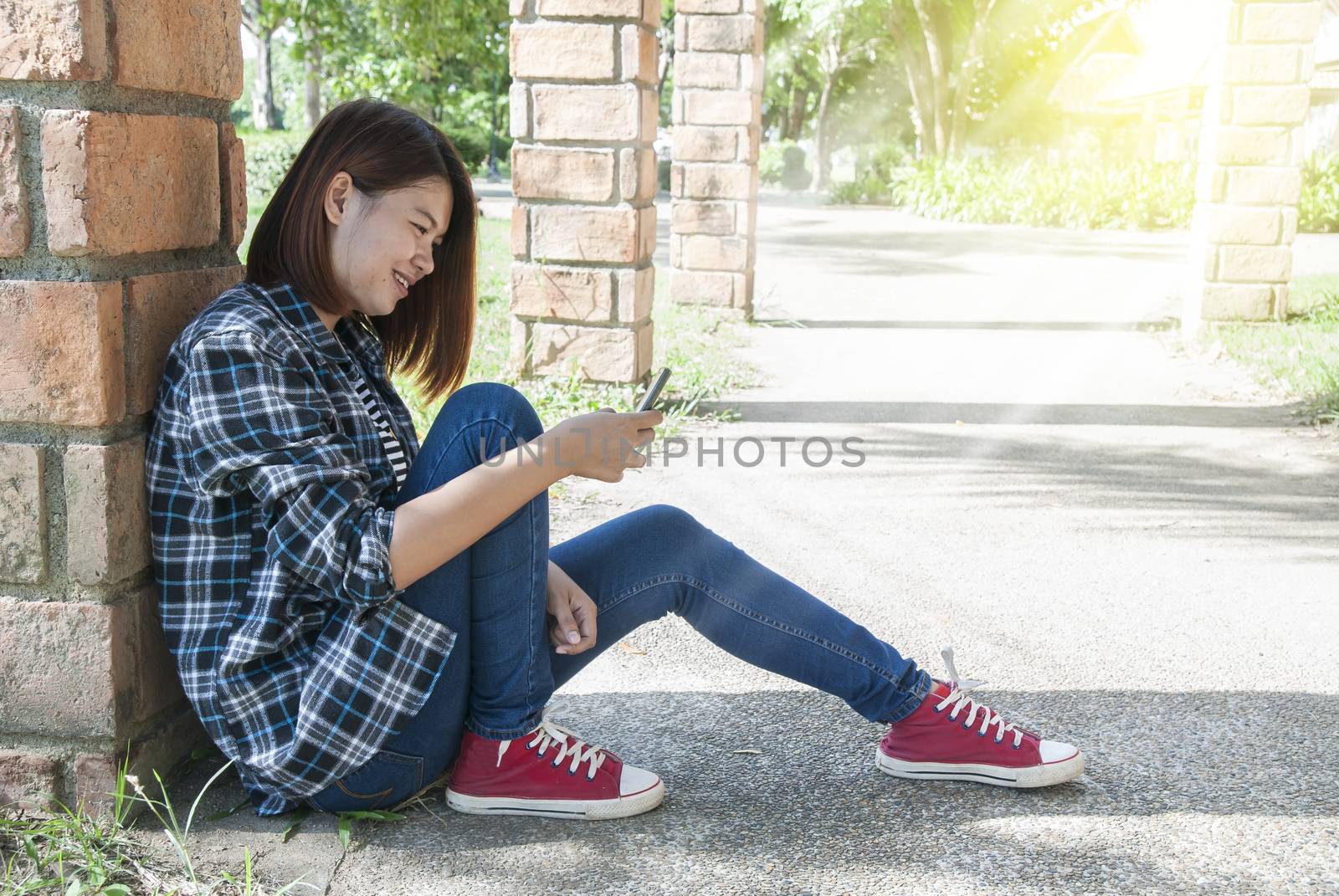 young woman smiling using her phone in park with sunlight