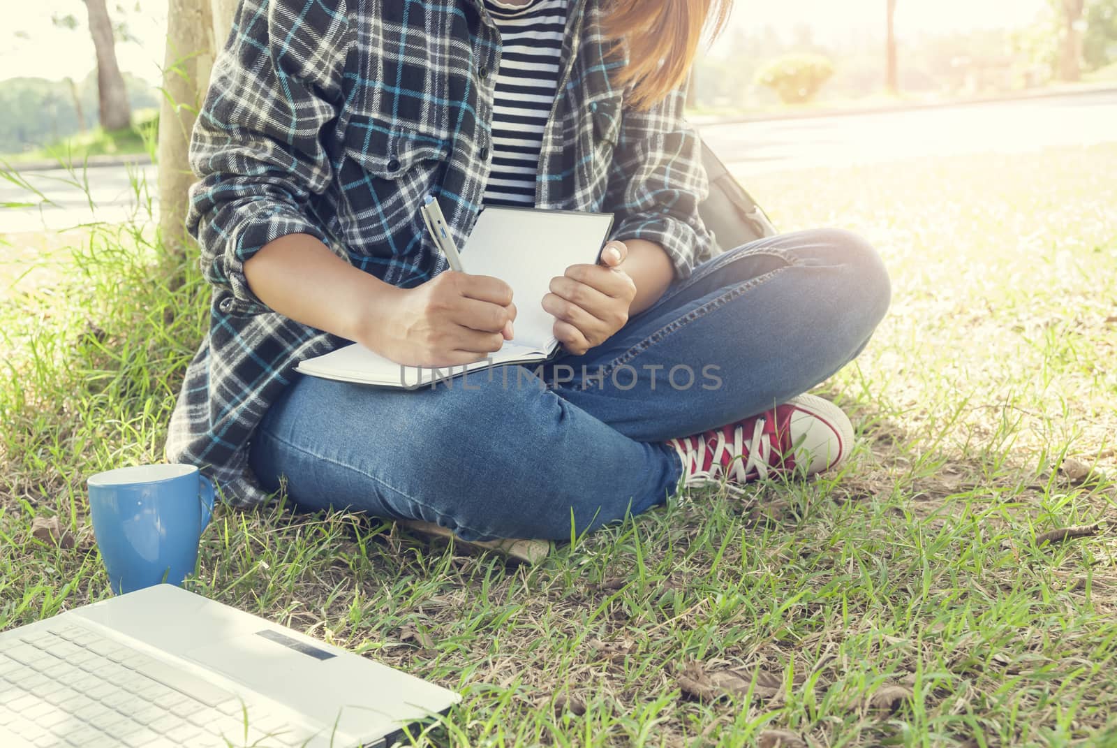 young woman sitting writting notebook at park