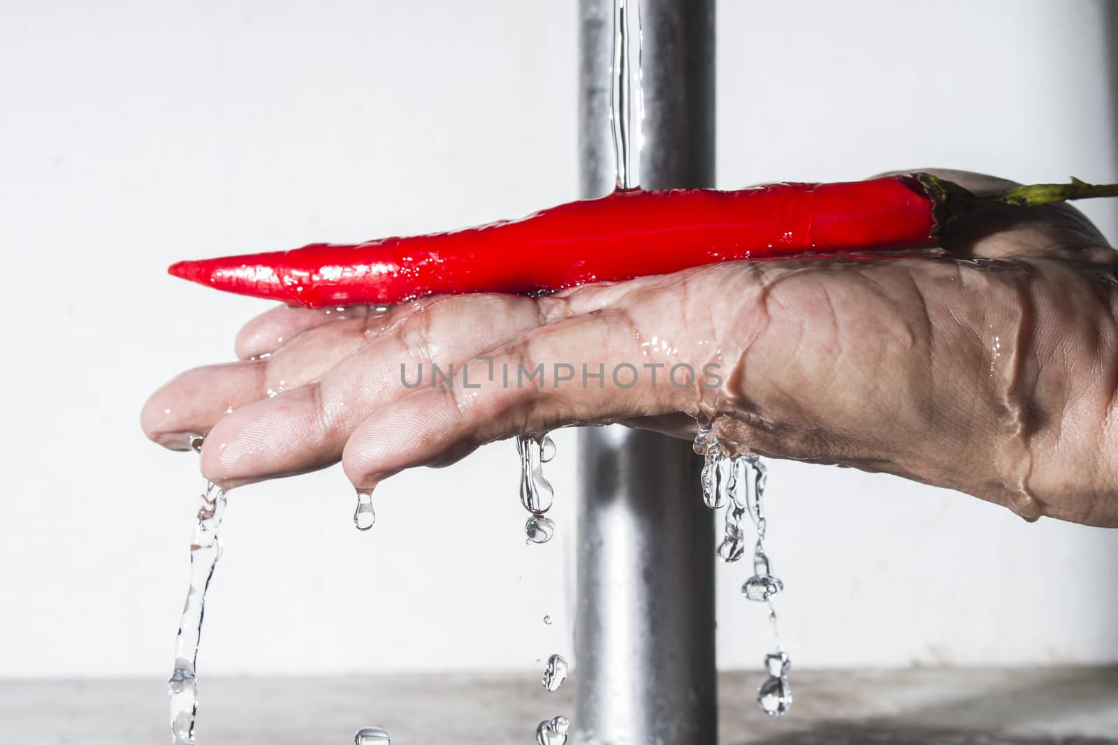 Red chilli pepper on male hand cleaning with falling water