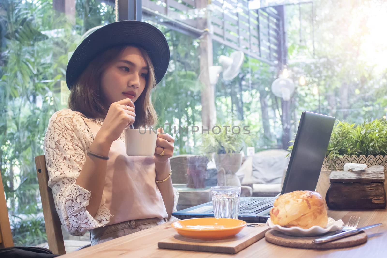 Asian women holding coffee cup looking laptop in cafe by Gobba17
