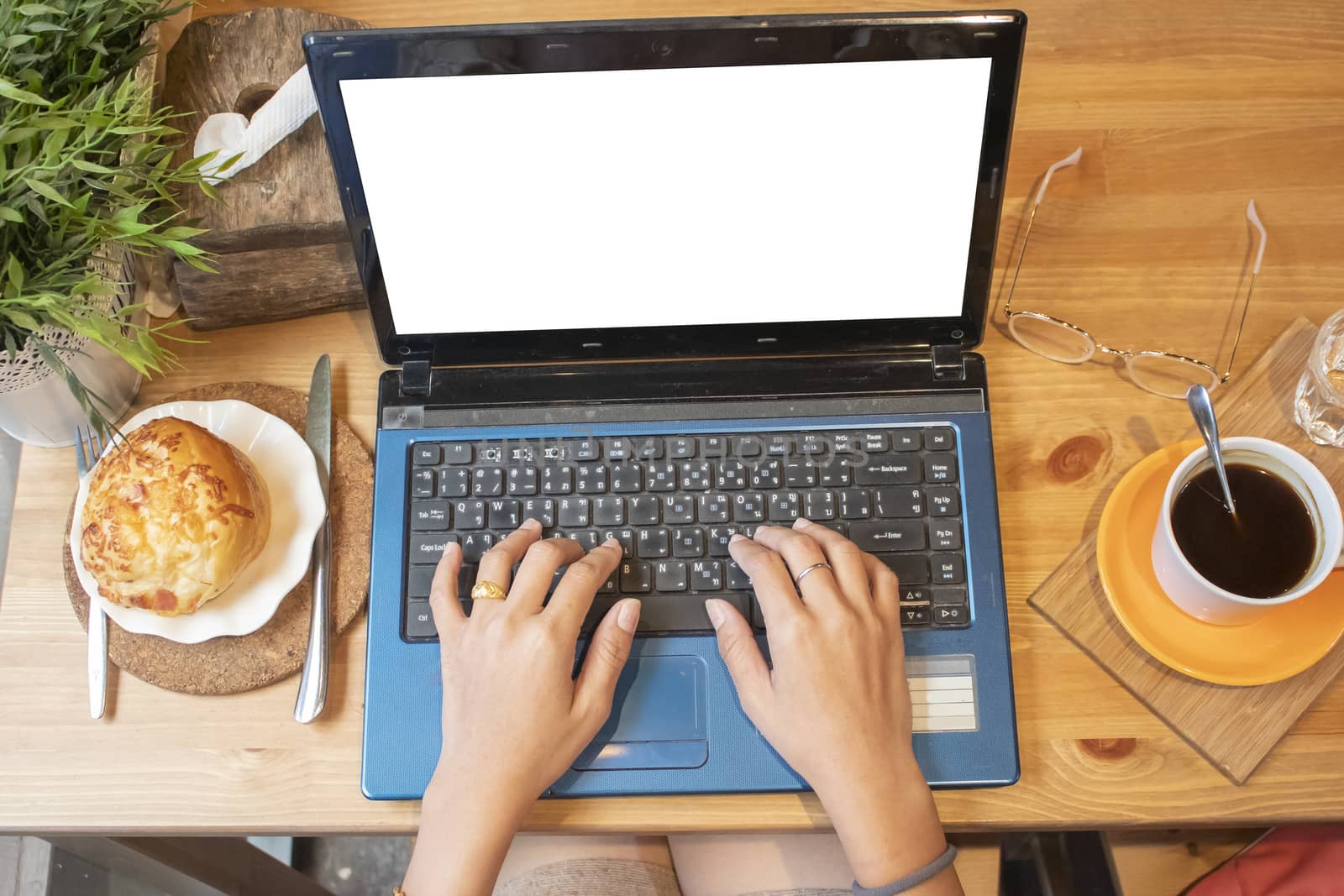 Top view of female using her laptop at a cafe. Overhead shot of young woman sitting at a table with a cup of coffee