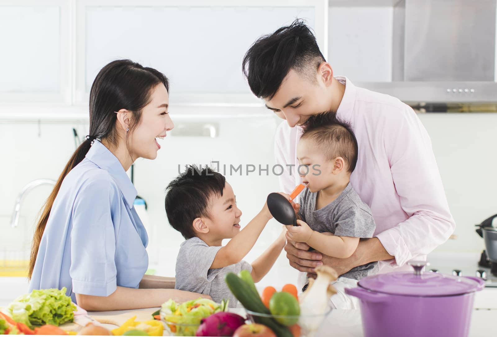 parent and boy feeding son a piece of carrot in kitchen by tomwang