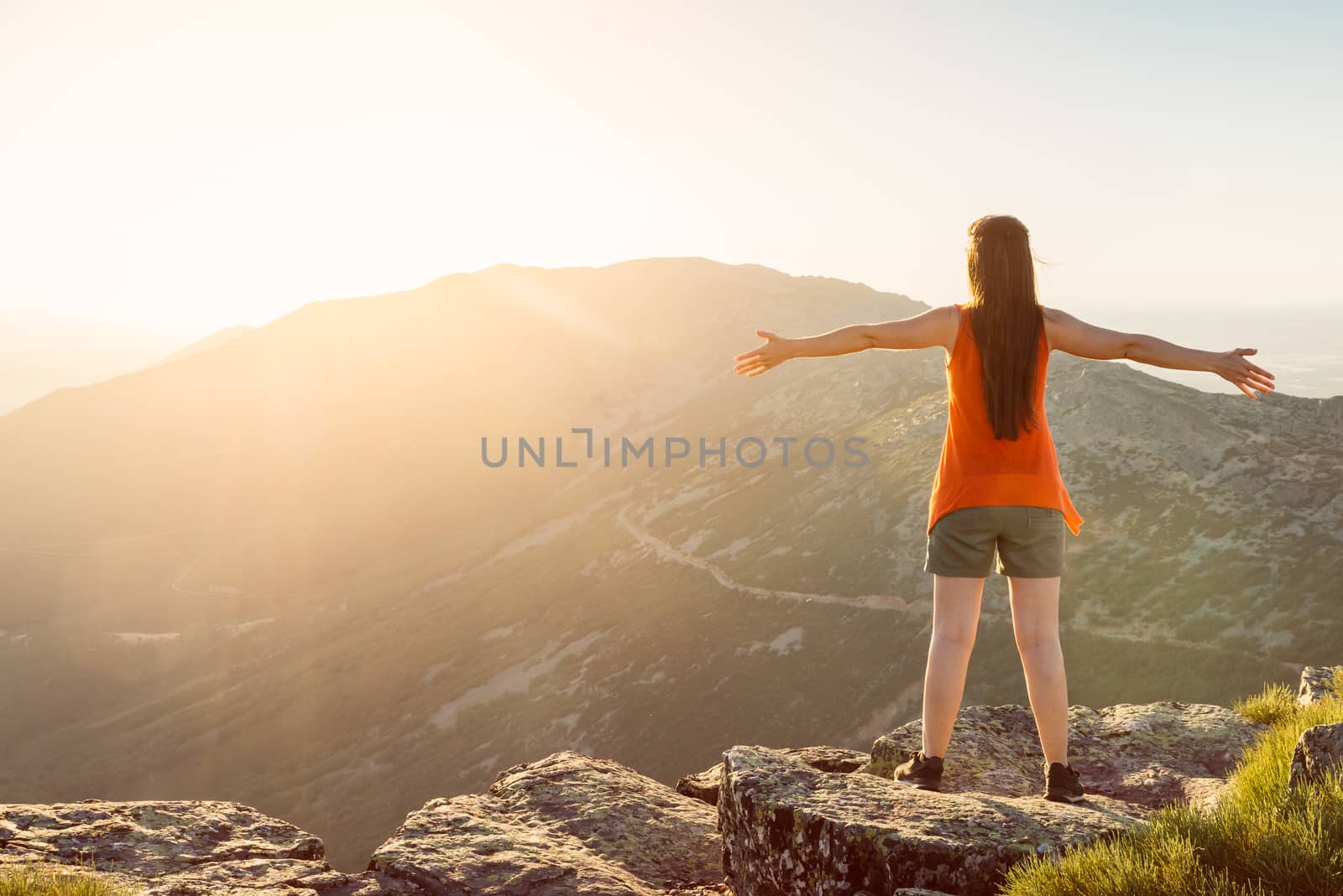 Happy woman with open arms stay on the peak of the mountain cliff edge under sunset light. by Fotoeventis