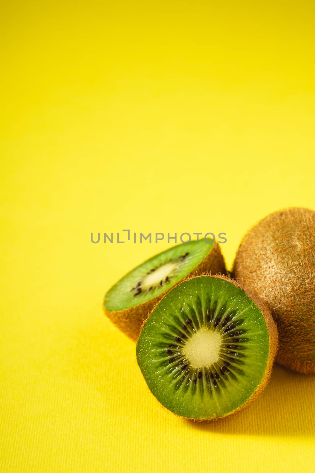 Kiwi fruits half sliced on vibrant plain yellow background, copy space, angle view