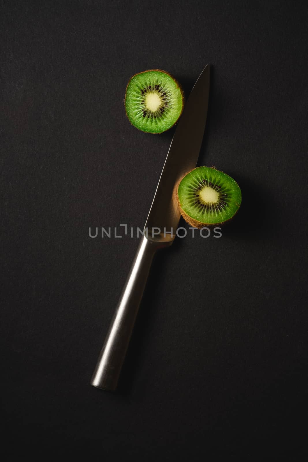 Kiwi fruits half sliced with kitchen knife on dark background
