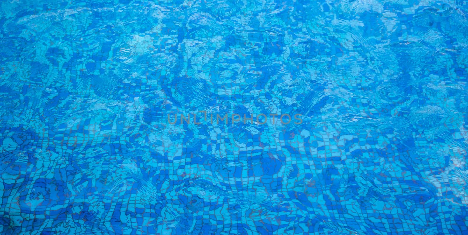 A pool with a mosaic bottom. Blue transparent water ripples. Space for text