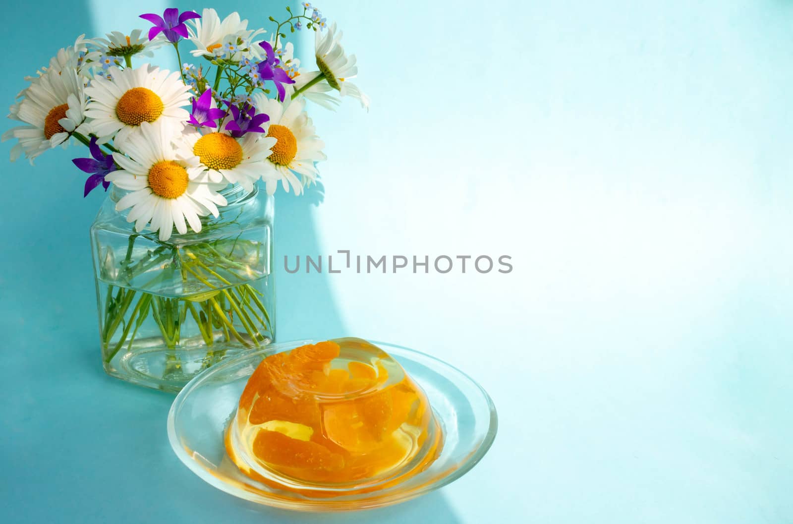 Breakfast jelly with tangerine slices and a bunch of daisies on a blue background.