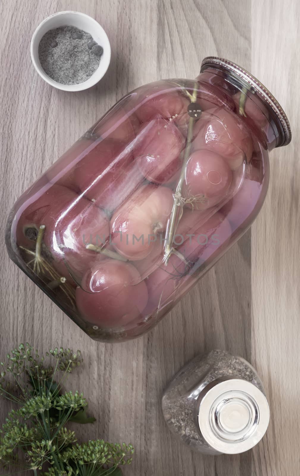 Home preservation: a large glass jar with red ripe pickled tomatoes, closed with a metal lid, next to spices and herbs. Top view, close-up.