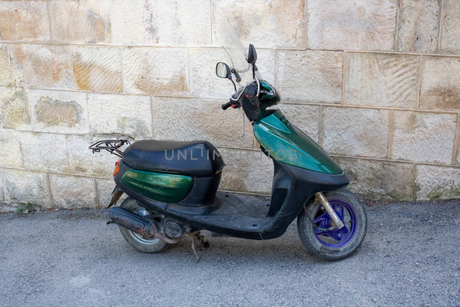 A green scooter is parked in an alley near a stone wall. Fast delivery