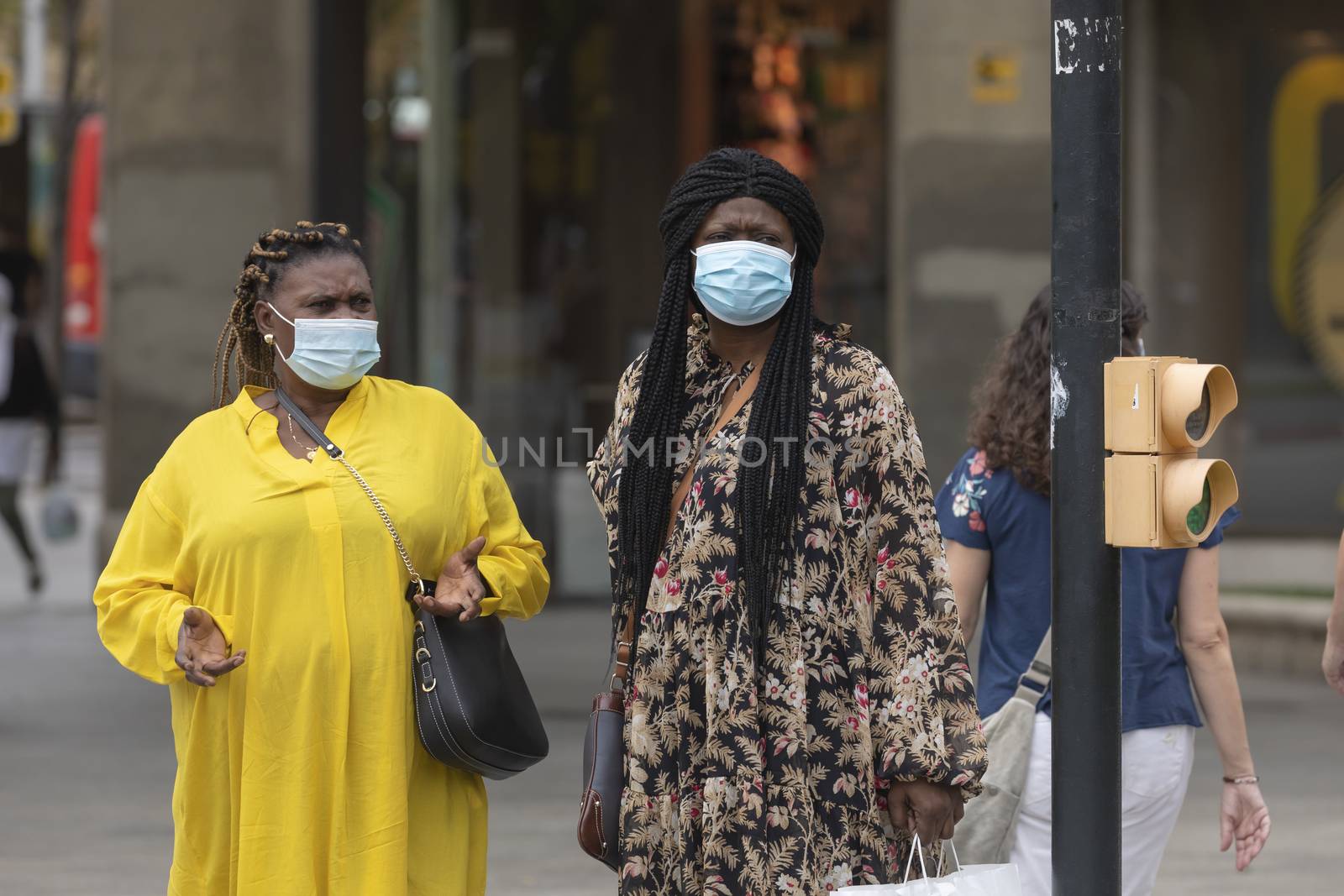 Zaragoza, Spain - August 18, 2020: Couple of black inmigrant women talking with face masks, due to the coronavirus pandemic, in the central area of Zaragoza.