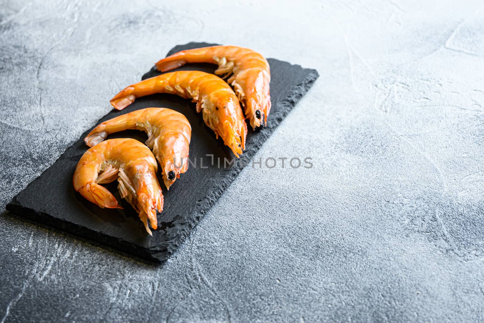 Raw ingredients shrimp on a stone cutting board over textured grey white backgrounnd, top view, closeup space for text.